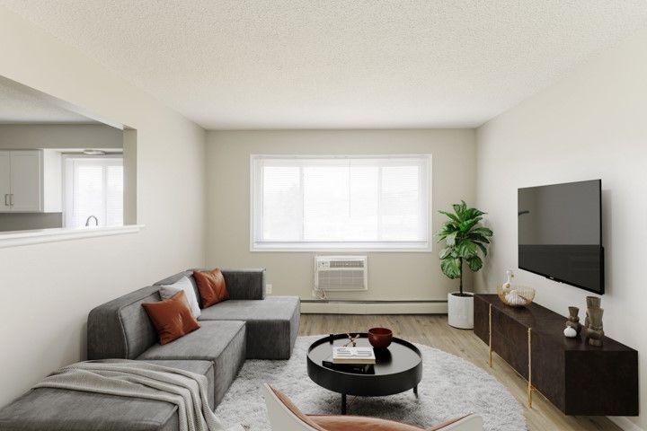 Bright living room with gray sectional, round coffee table, wall-mounted TV, and large window.