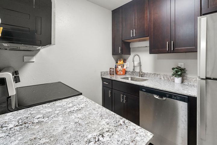Modern kitchen with dark cabinets, granite countertops, stainless steel appliances, and a black cooktop
