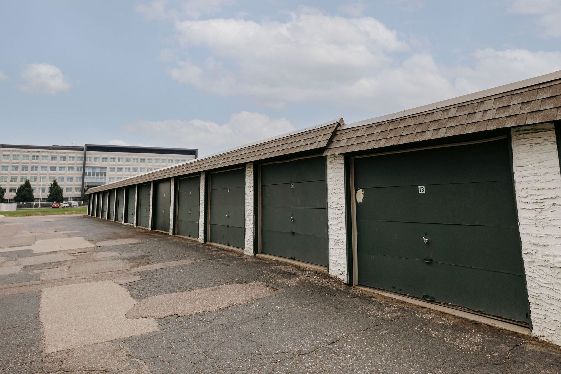 Row of green garage doors along a paved alley beside a building under a cloudy sky