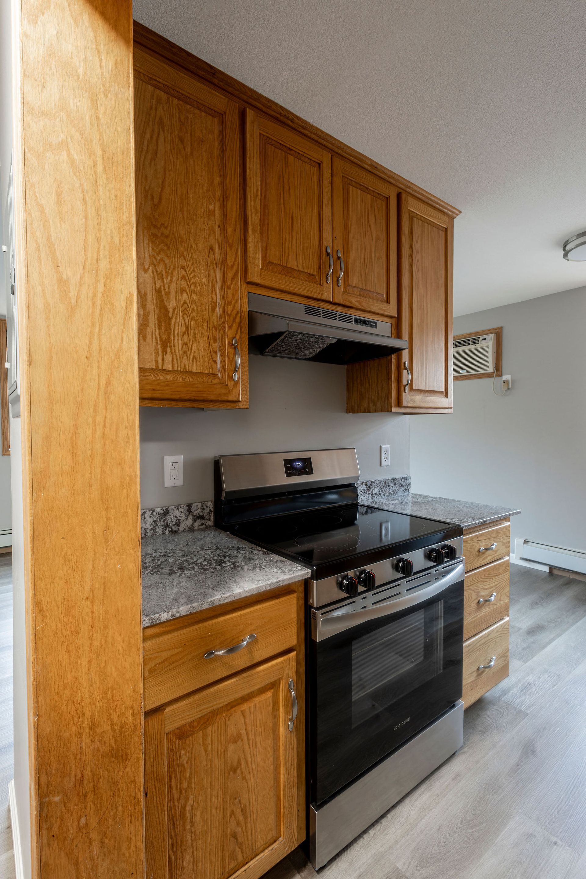 Kitchen with oak cabinets, black stove, speckled countertop, and light wood flooring