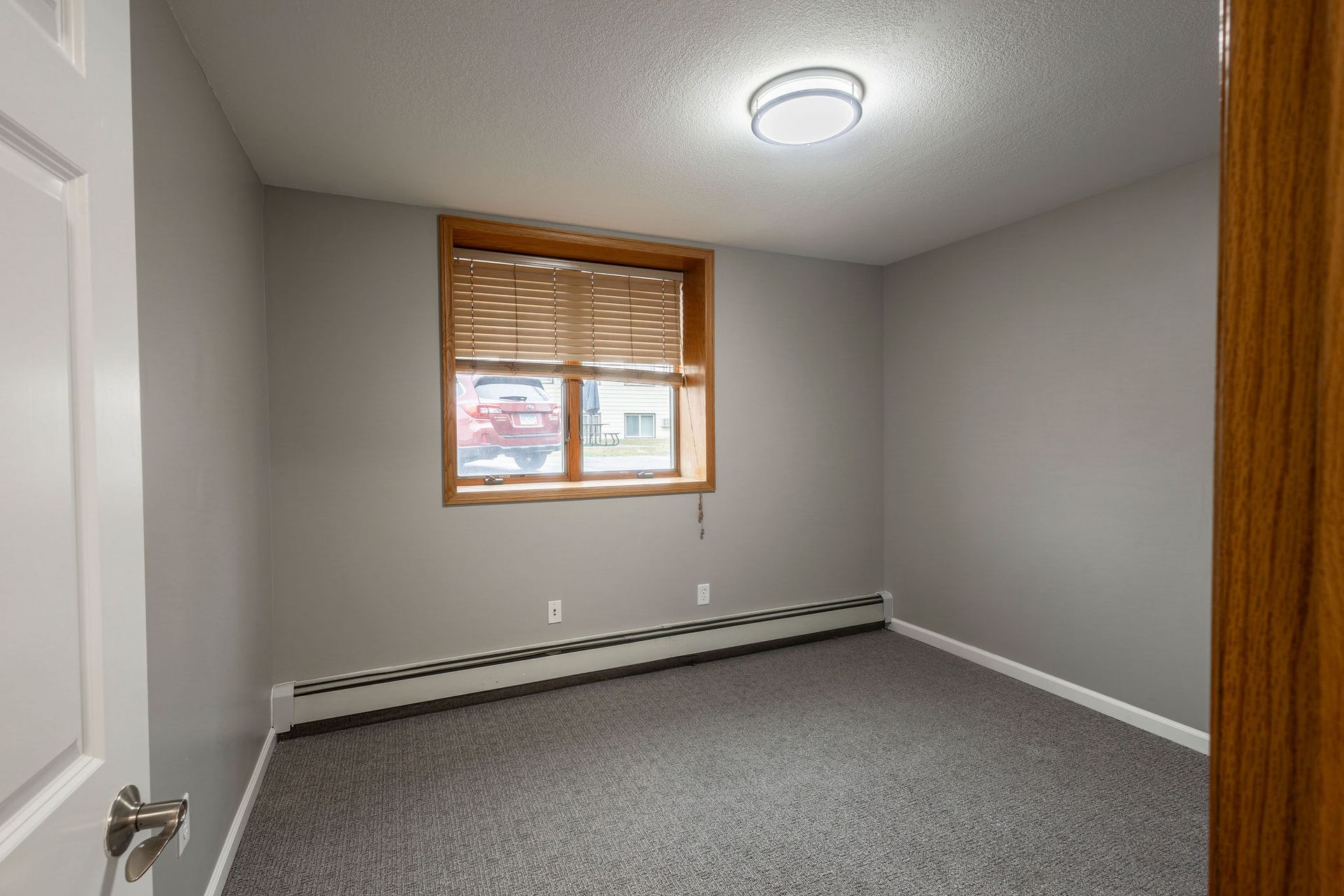 Empty gray bedroom with carpet, window blinds, and a ceiling light