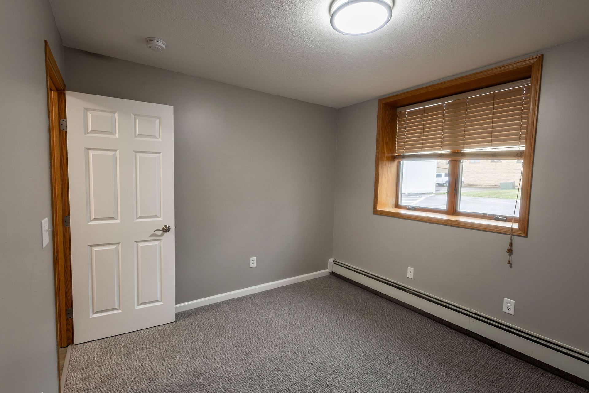 Empty gray bedroom with carpet, white door, and window with wooden blinds.