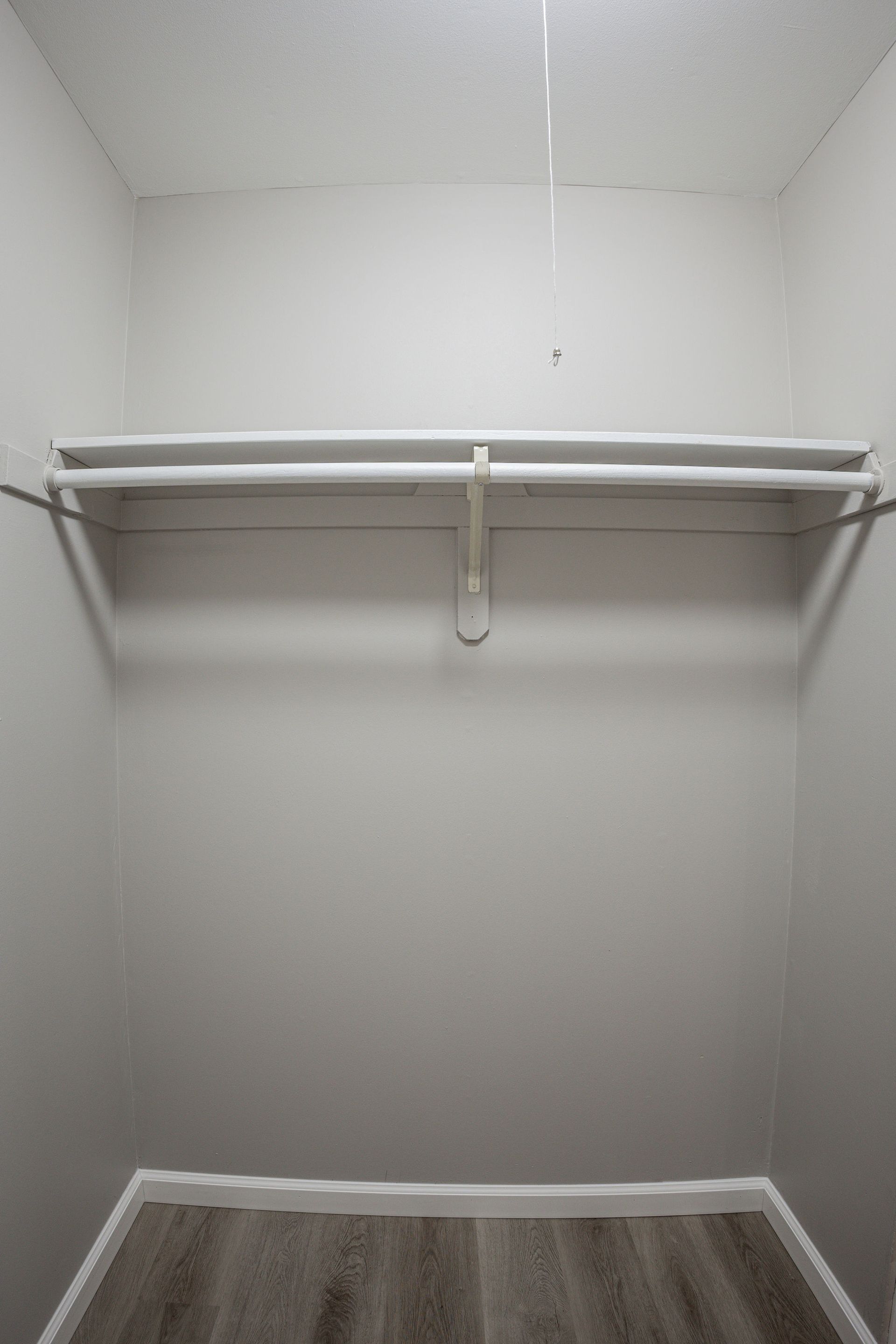 Empty walk-in closet with white walls, shelves, and hanging rod over wood flooring.