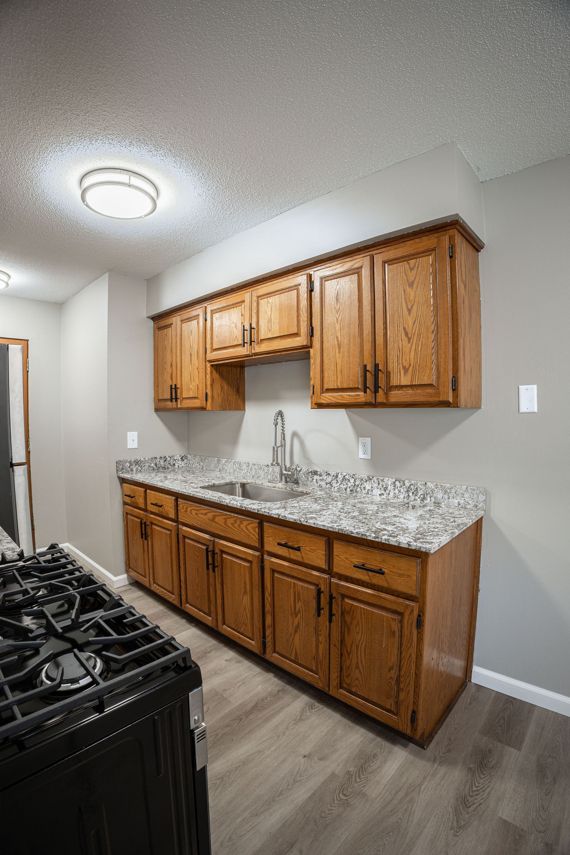 Kitchen with oak cabinets, granite countertop, sink, and stove under a textured ceiling light.