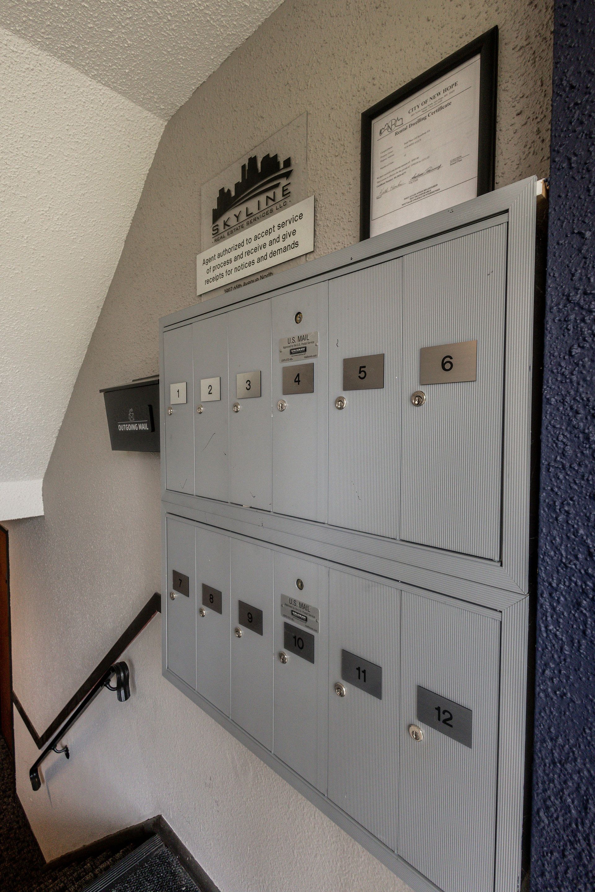 Row of gray apartment mailboxes mounted on a stairwell wall with framed notices above them