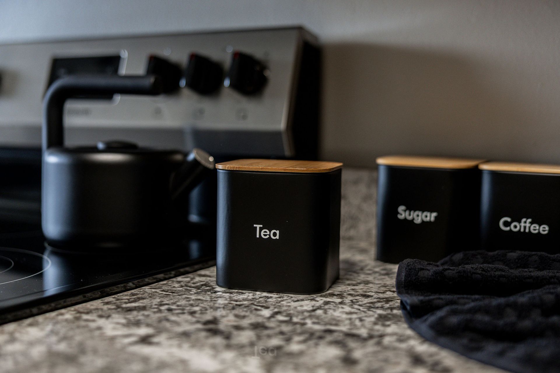 Black kitchen canisters labeled tea, sugar, and coffee on a granite countertop