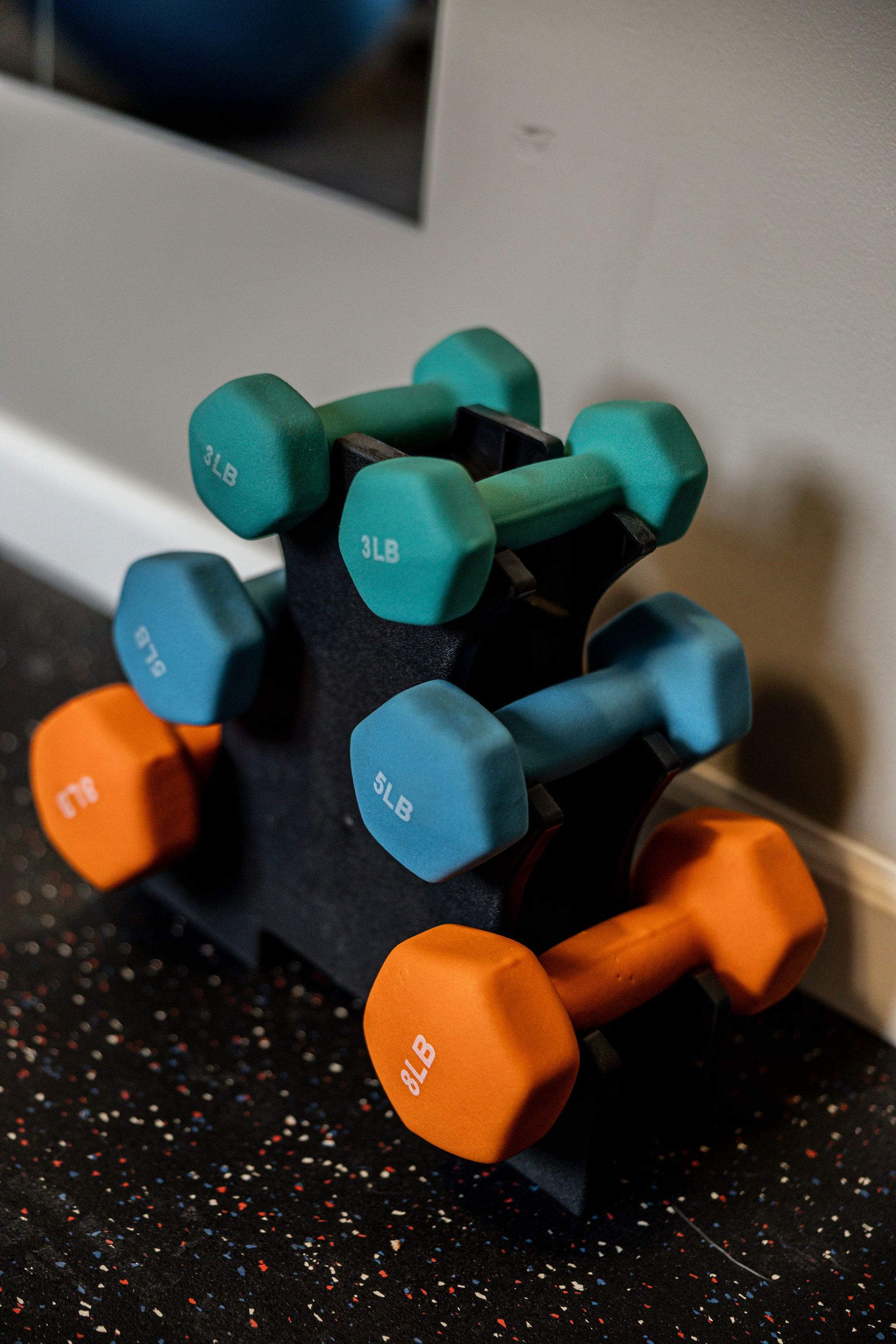 Colorful dumbbells stacked on a rack against a wall in a gym corner
