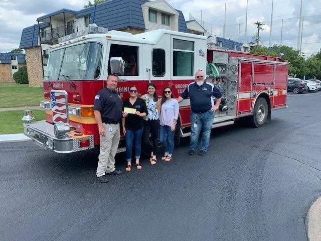 Five people standing in front of a red fire truck on a residential street.
