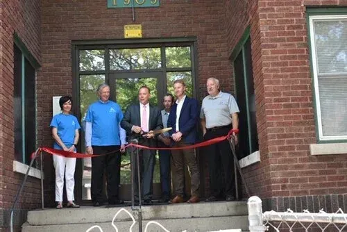 People cutting a red ribbon at a brick building entrance