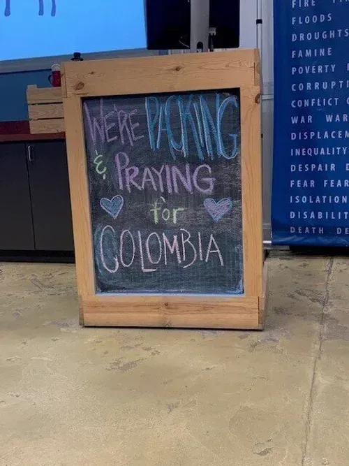 Wooden signboard reading “We’re voting & praying for Colombia” in pastel chalk outside a building