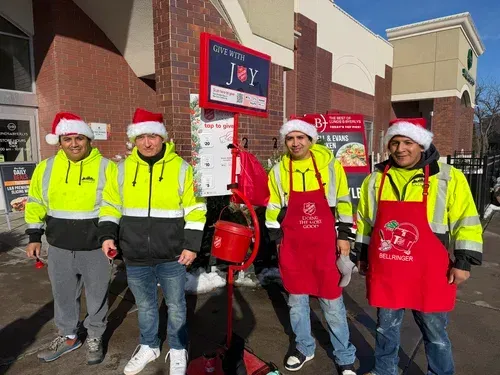 Five volunteers in Santa hats stand outside a store, wearing neon safety jackets and holding donation buckets.
