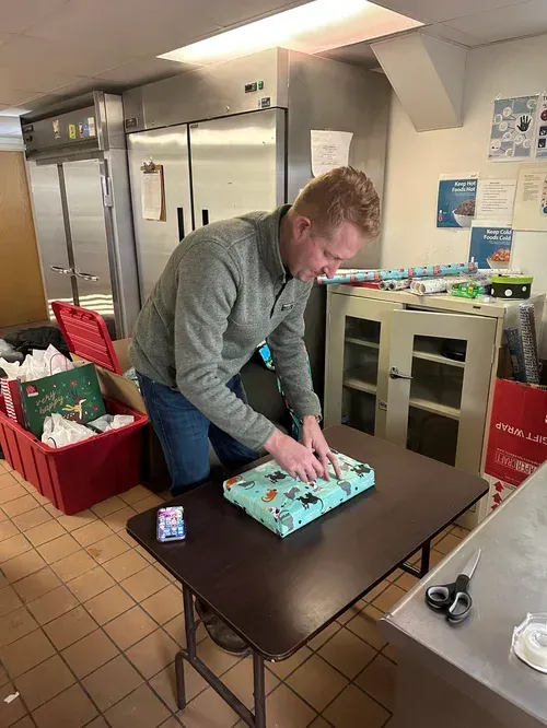 Person wrapping a turquoise gift at a table in a kitchen-like room
