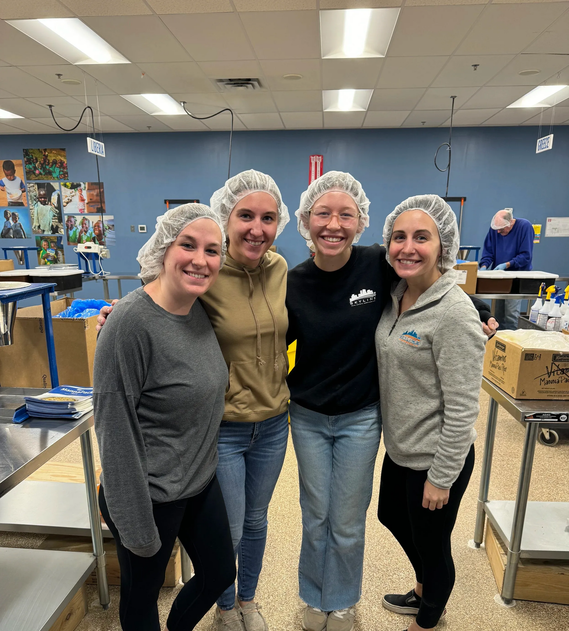 Four smiling people in hairnets pose together in a bright classroom or kitchen setting.