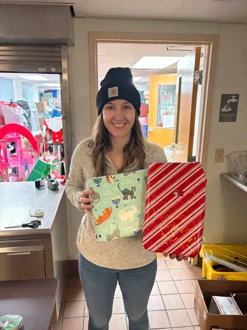 Woman in a room holding two wrapped gifts, one mint green and one red striped.