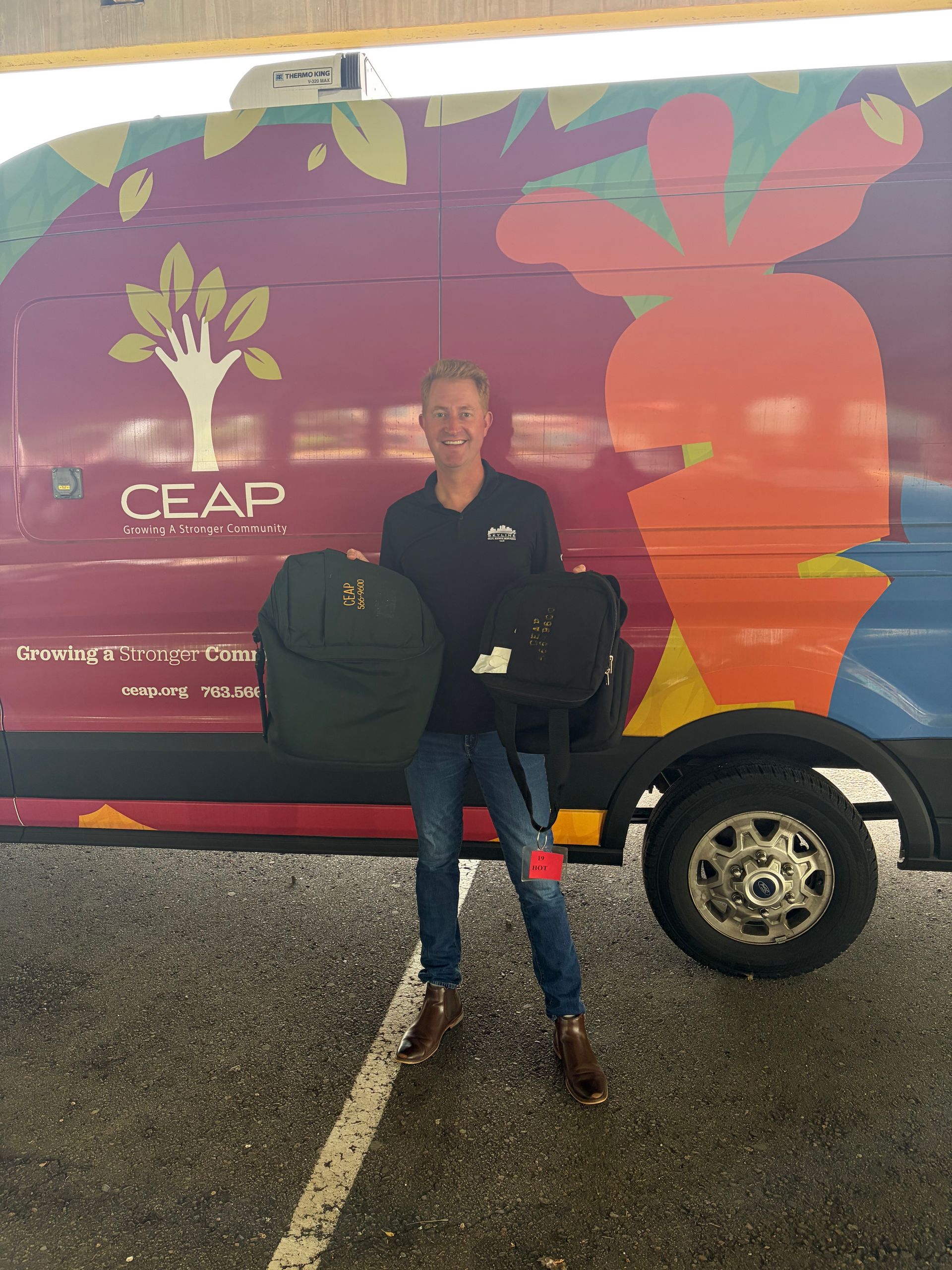 Person standing beside a colorful CEAP van in a rainy parking lot, holding a black bag.