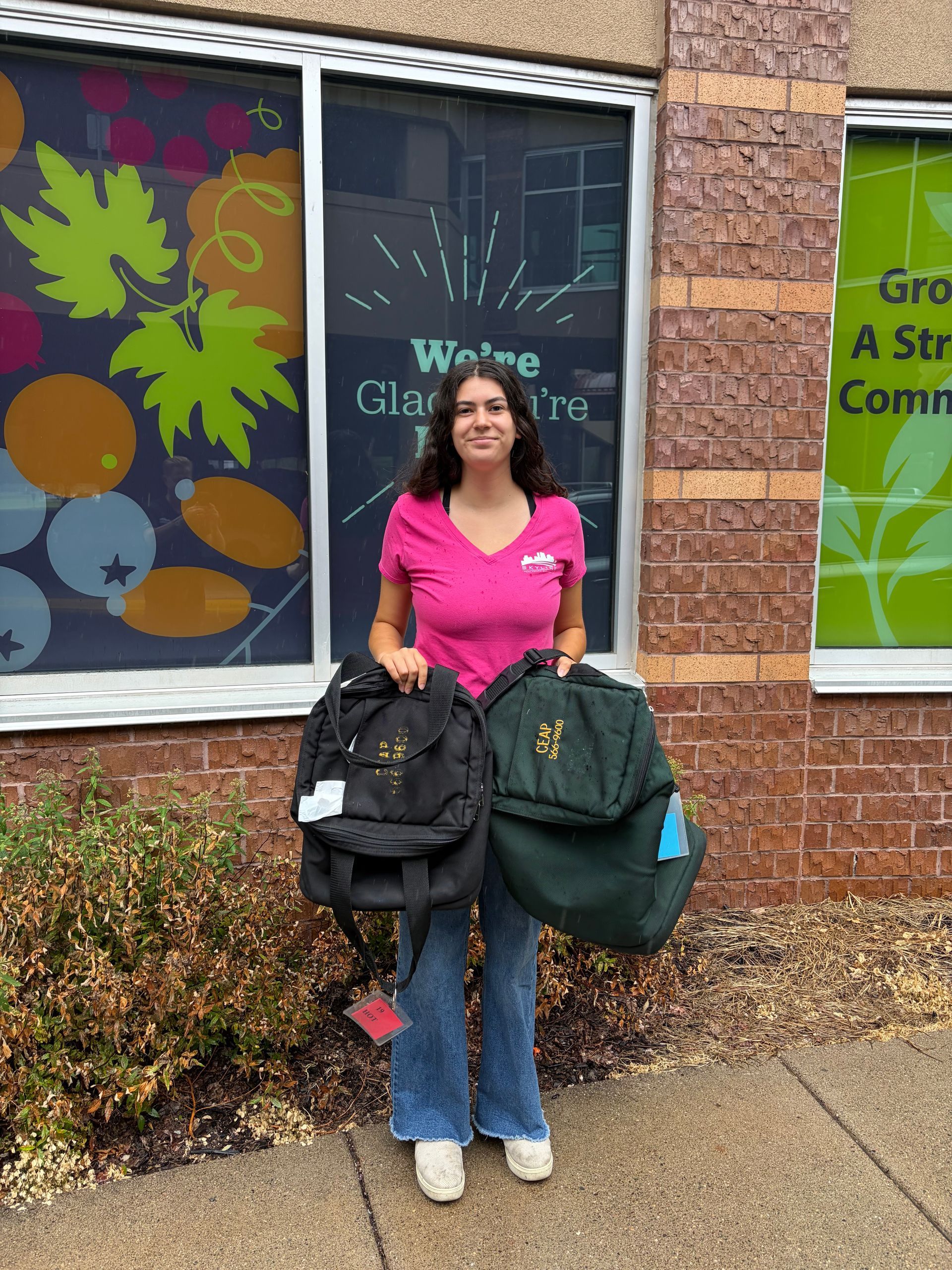 Woman holding two backpacks outside a building with colorful window art