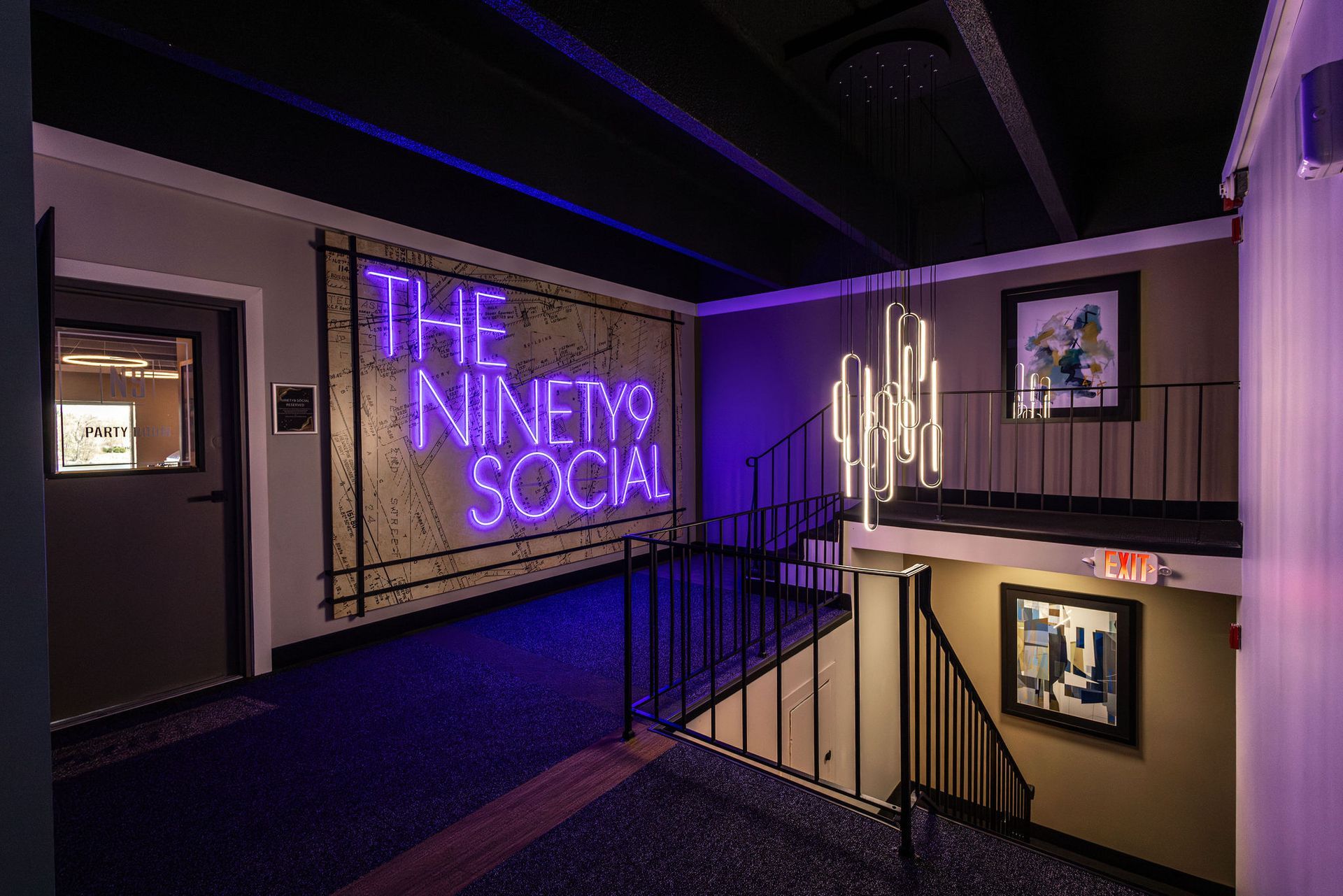 Purple neon sign reading “The Ninety Nine Social” in a dim, modern stairwell hallway