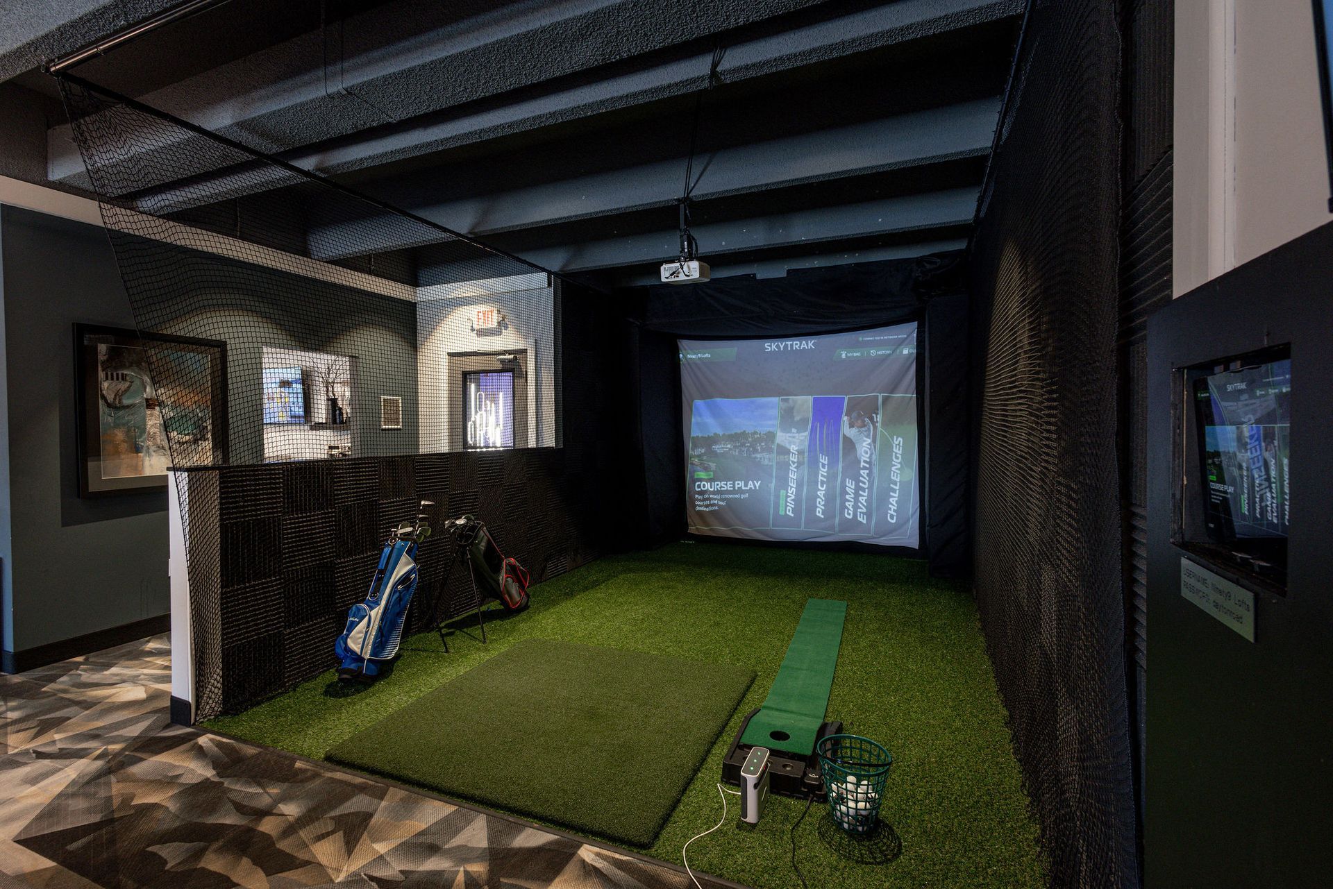 Indoor golf simulator with a projected course, putting turf, and clubs in a dark room