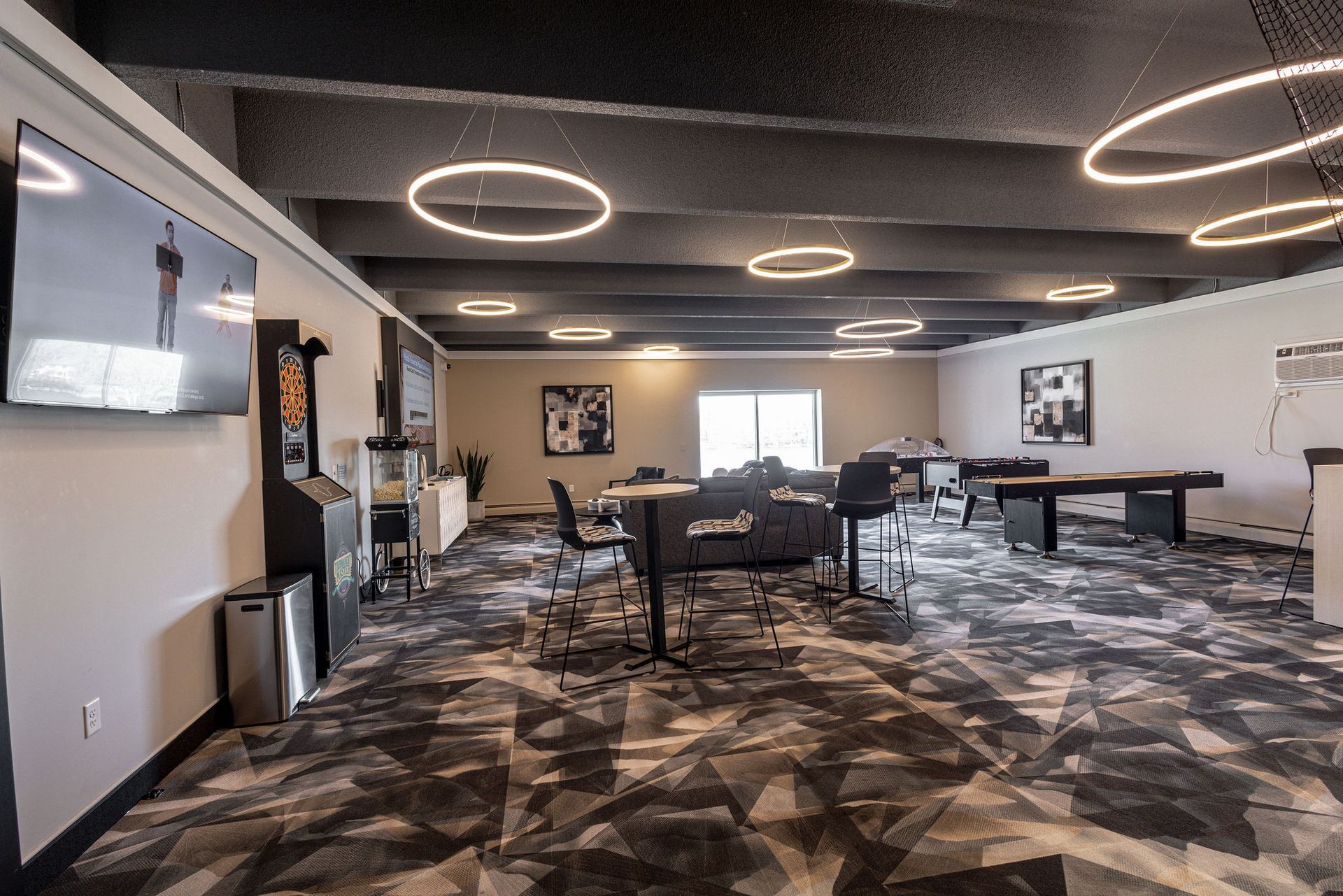 Modern lounge with patterned carpet, circular ceiling lights, TVs, tables, and a bar area.