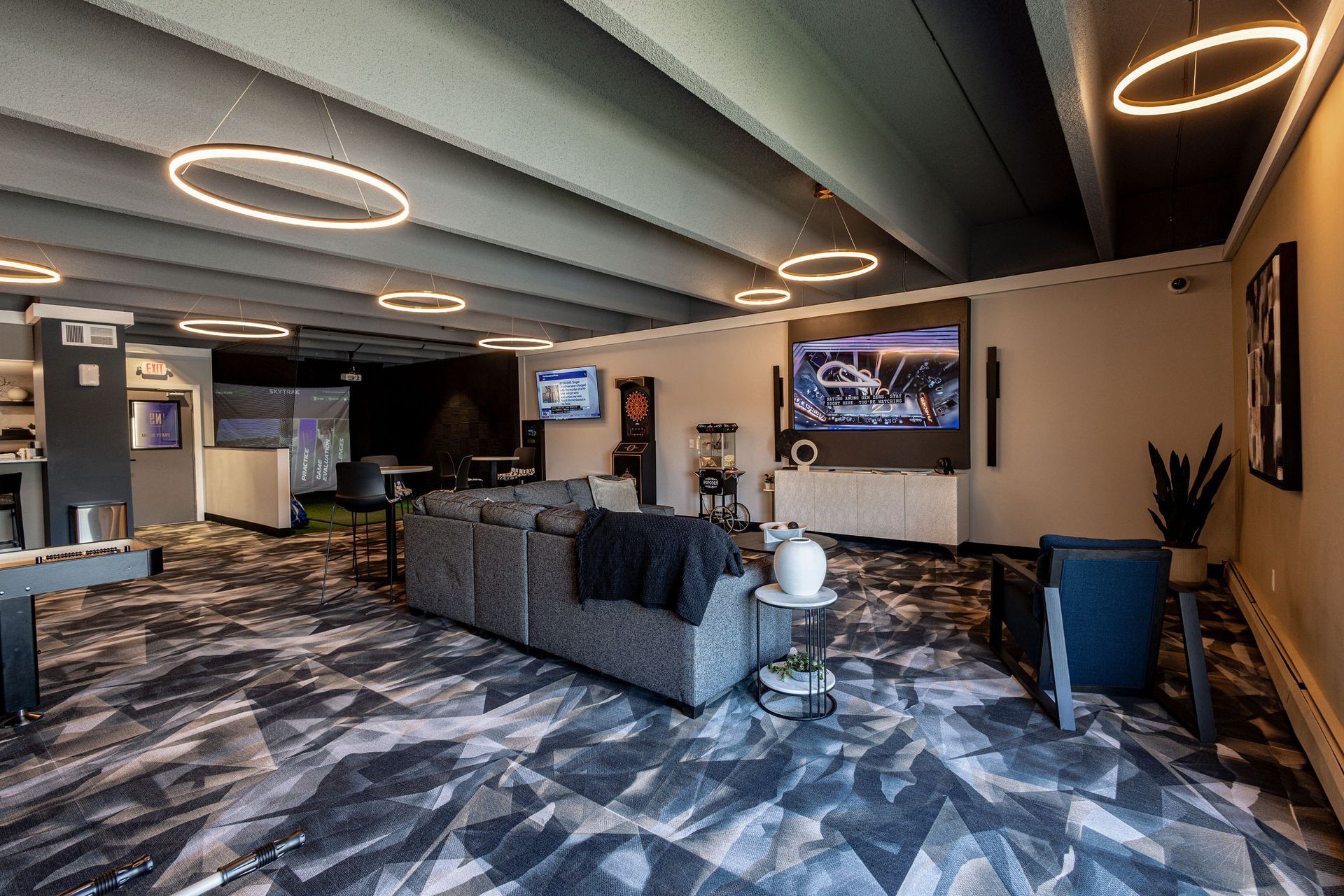 Modern lounge with gray sofas, patterned carpet, circular ceiling lights, and a wall-mounted TV