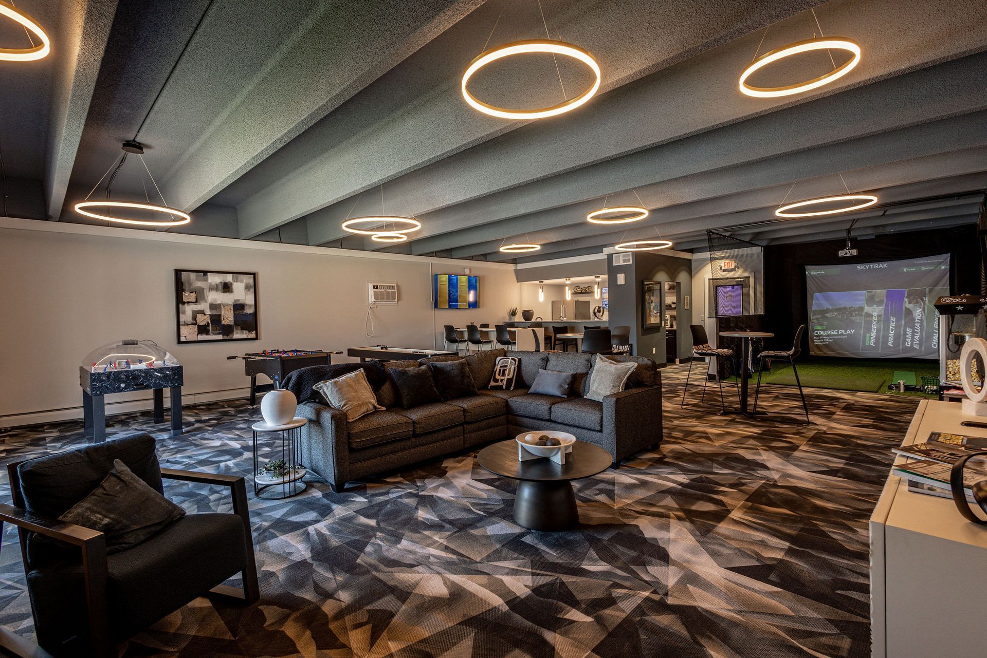 Modern lounge with couches, patterned carpet, circular ceiling lights, and a large TV screen