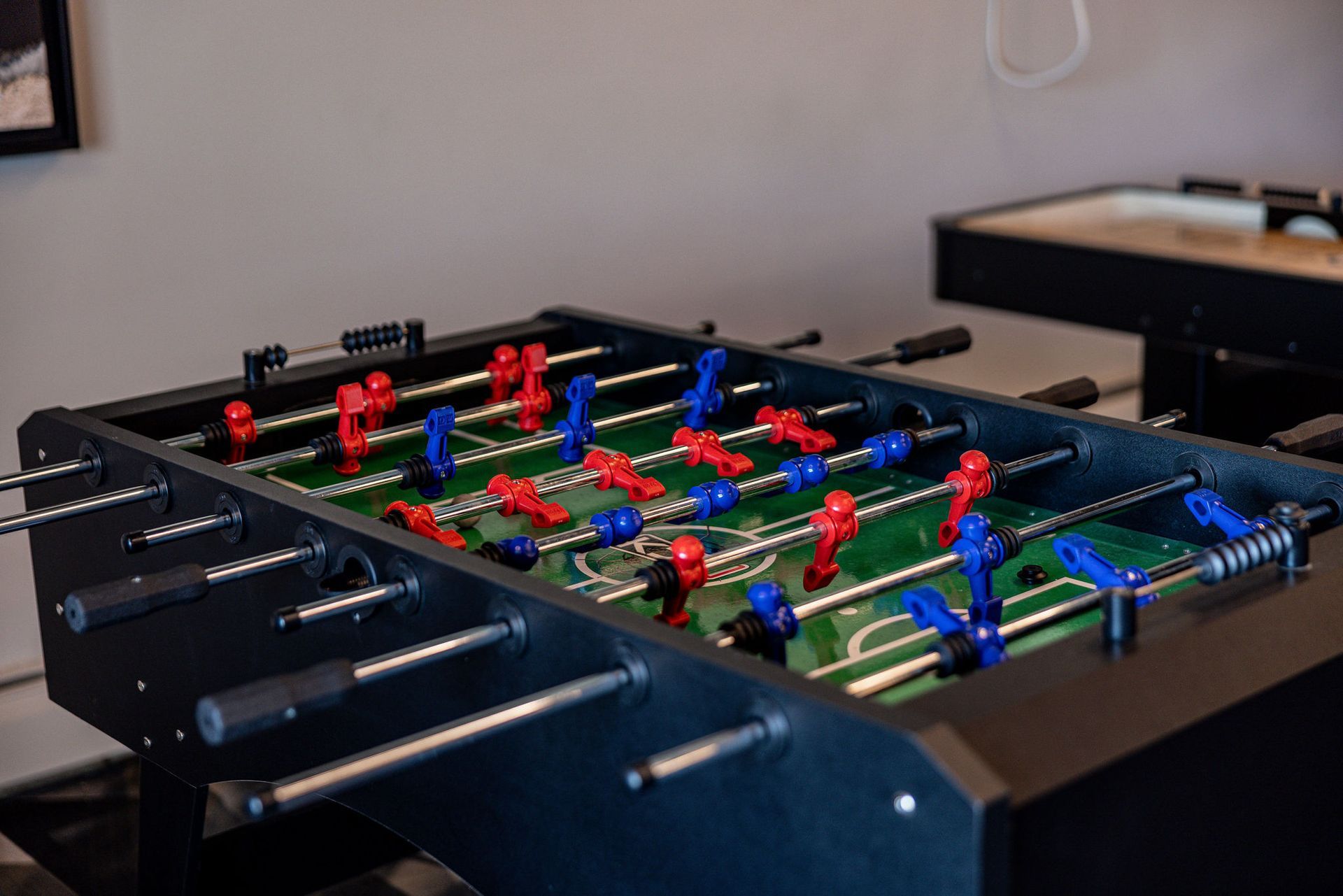 Foosball table with red and blue players on a green field in a room