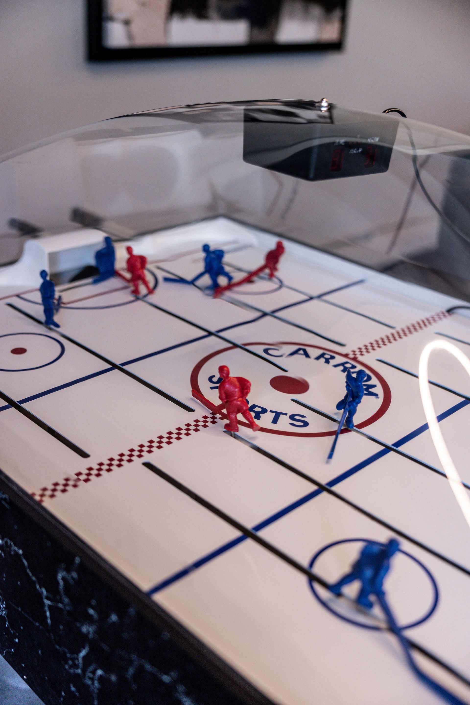 Miniature hockey figures on a tabletop rink with red and blue players near the goal.