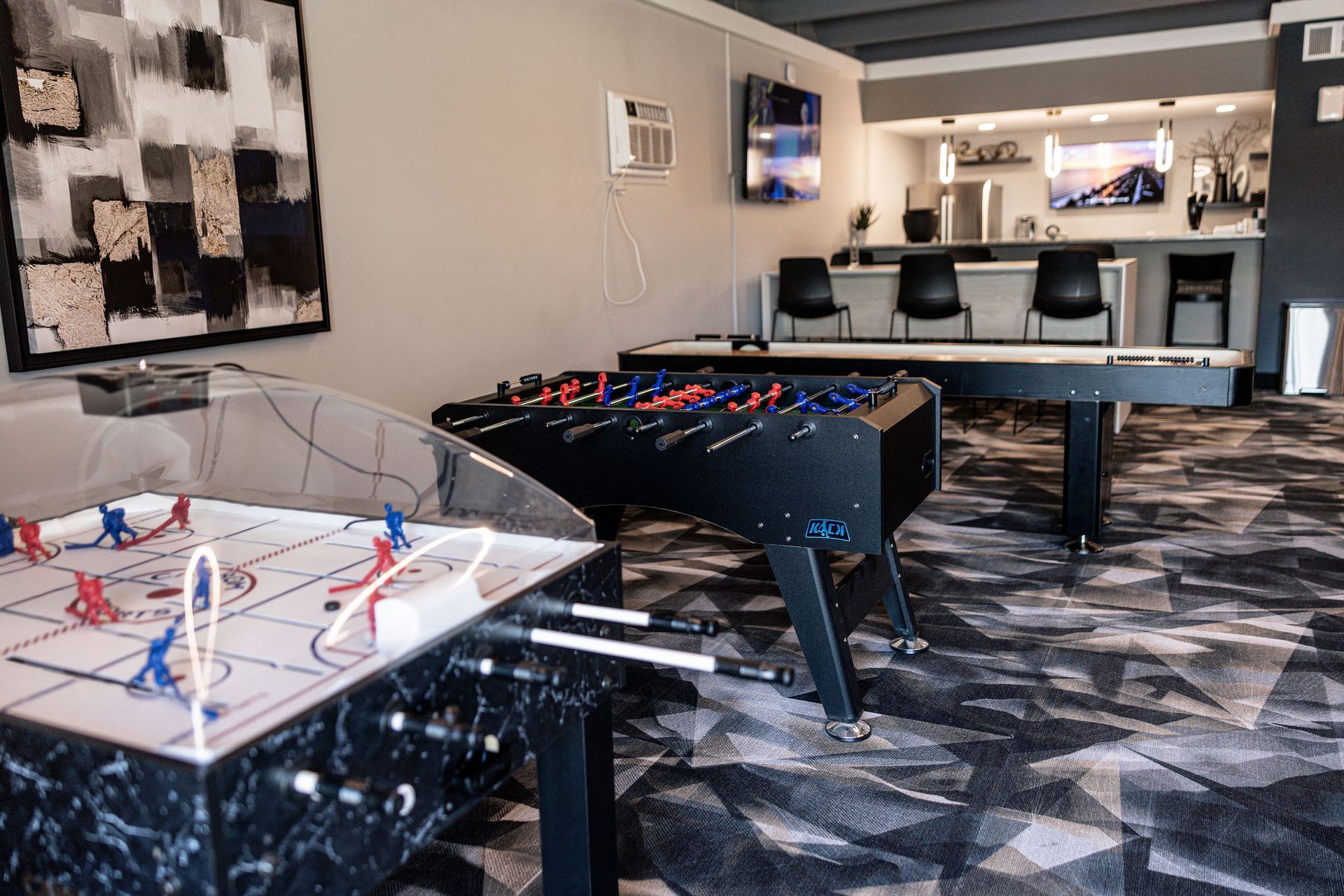 Game room with foosball table, air hockey table, and a bar with stools and TV.