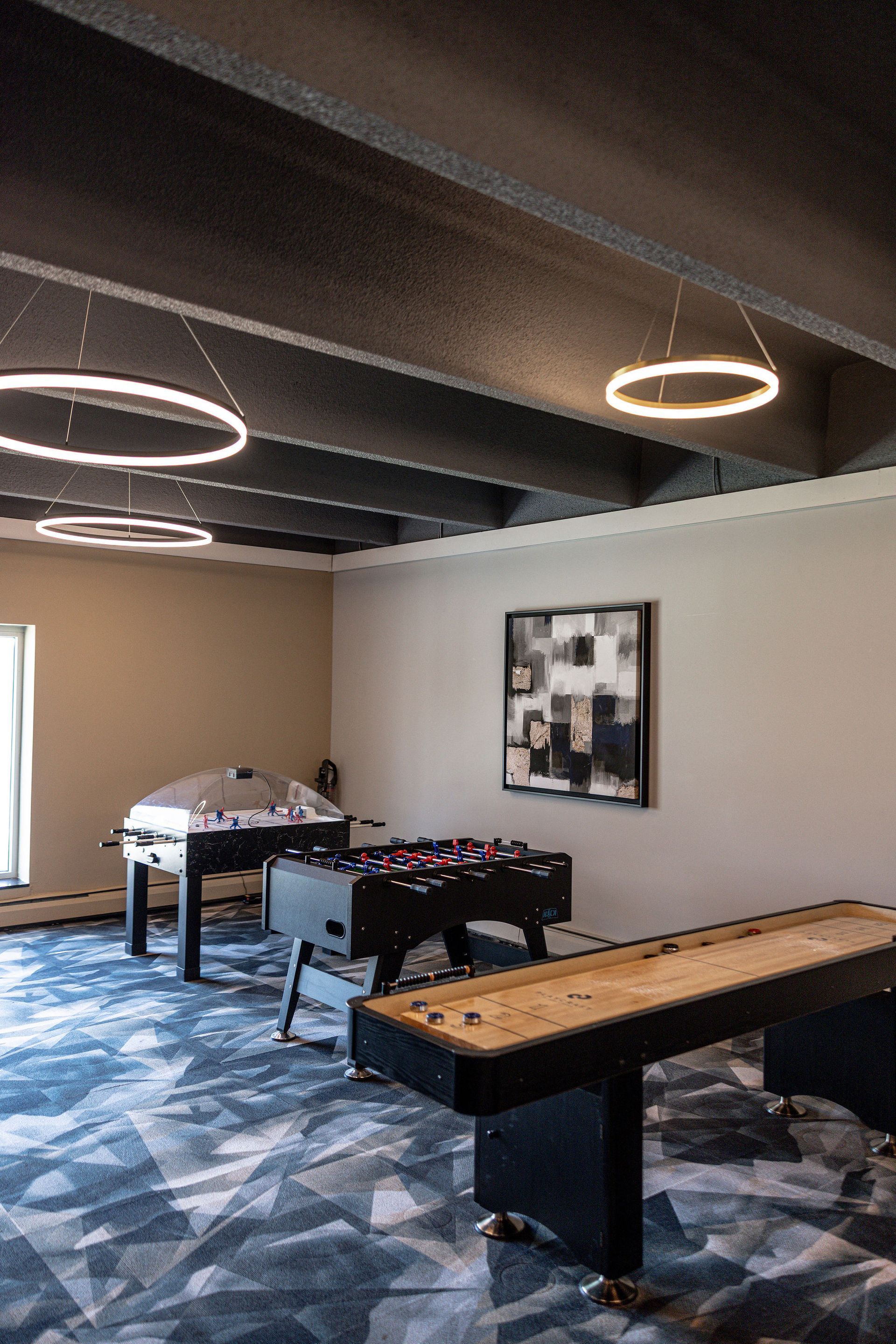 Game room with pool and foosball tables, blue patterned carpet, and modern ring ceiling lights.