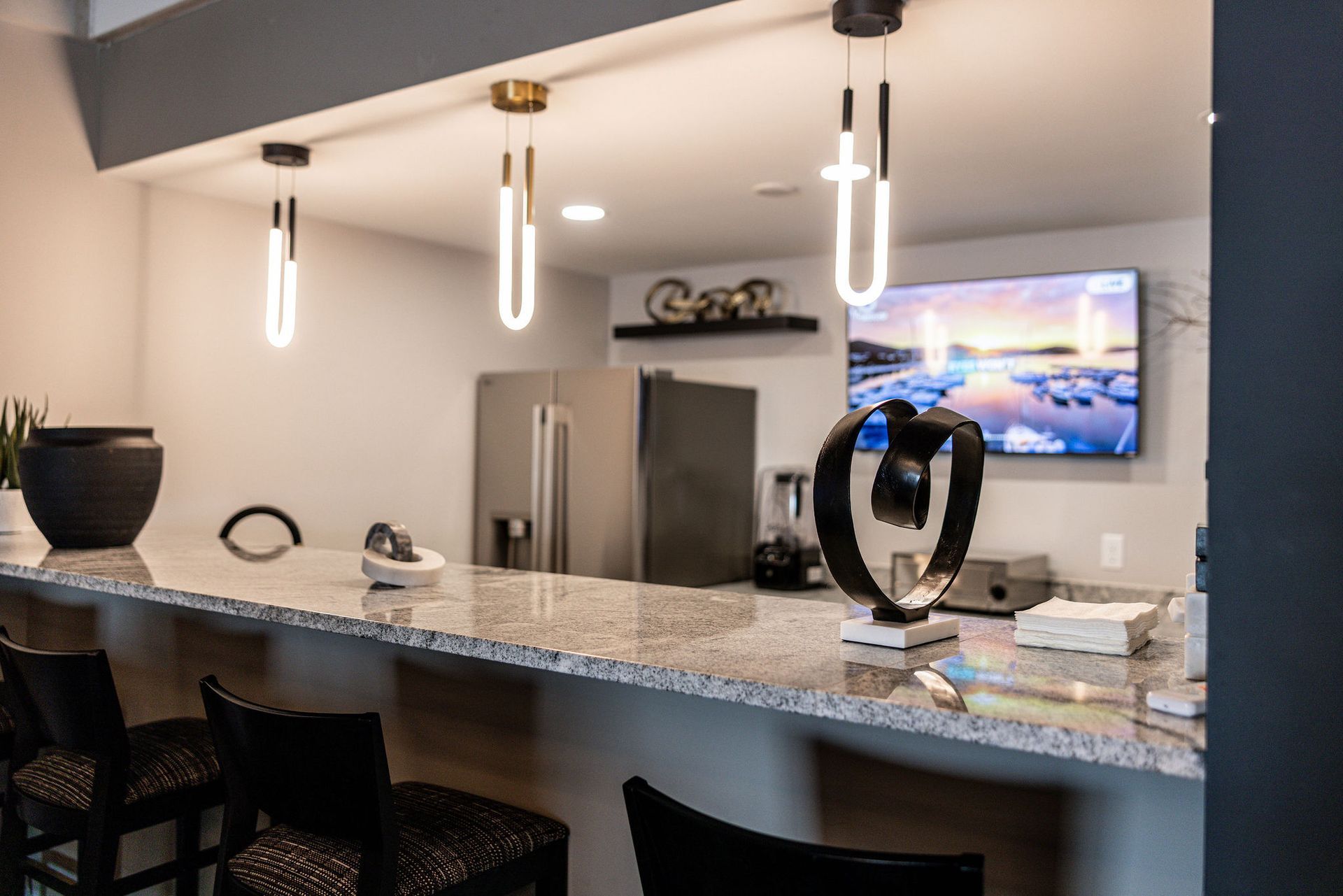 Modern kitchen with granite island, pendant lights, stainless steel fridge, and wall-mounted TV