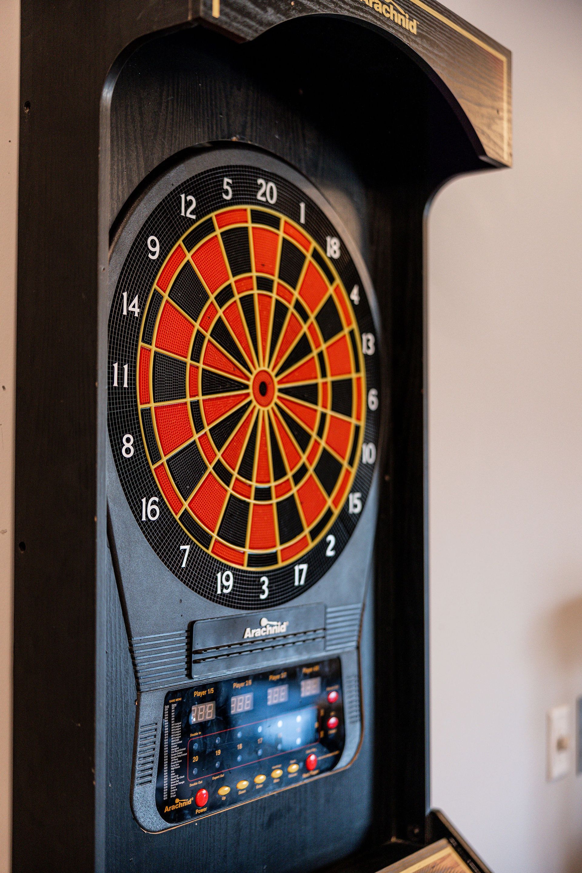 Electronic dartboard in a wall-mounted cabinet with a digital score display below.