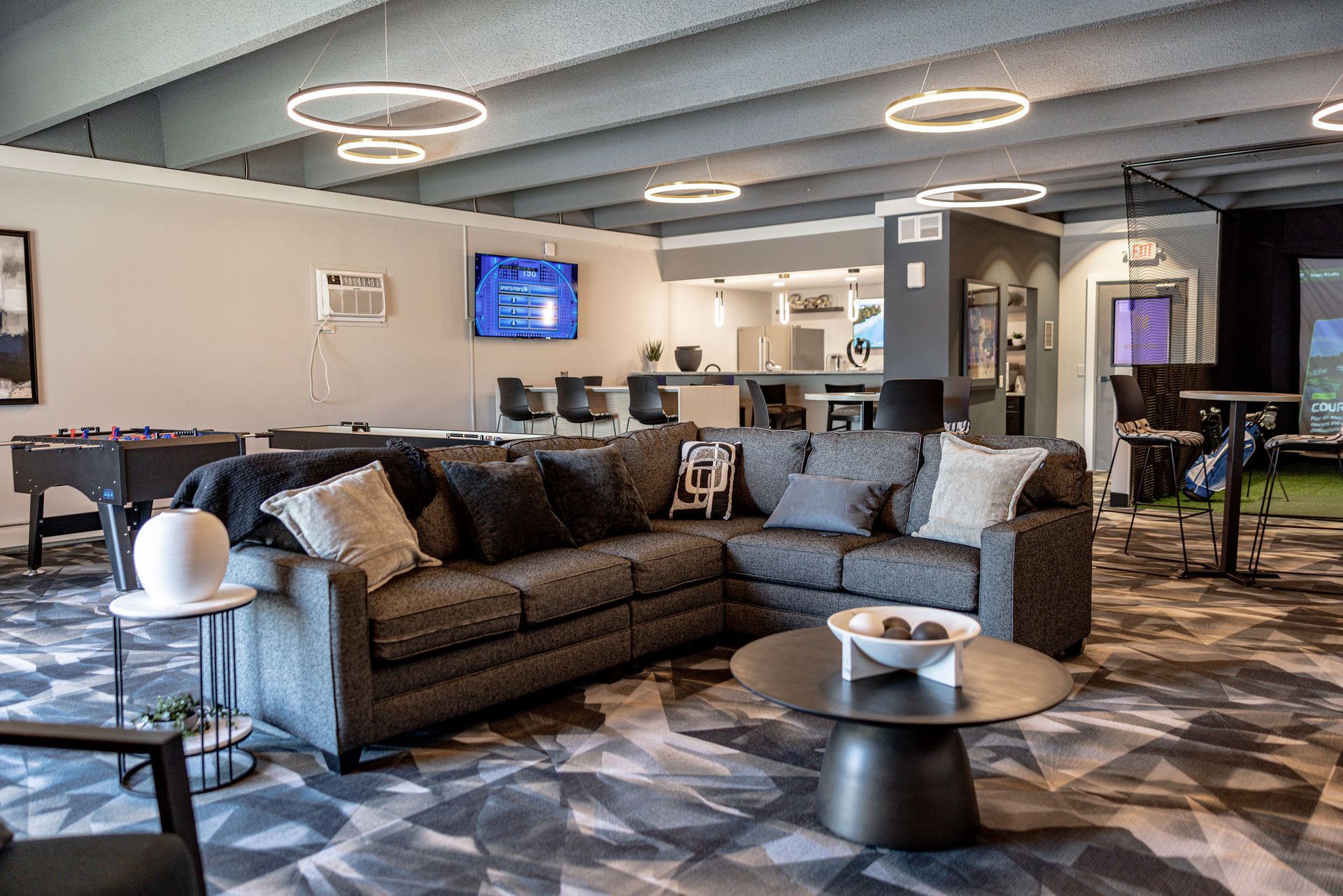 Modern lounge with gray sofas, circular ceiling lights, and a patterned carpet in an open office lobby