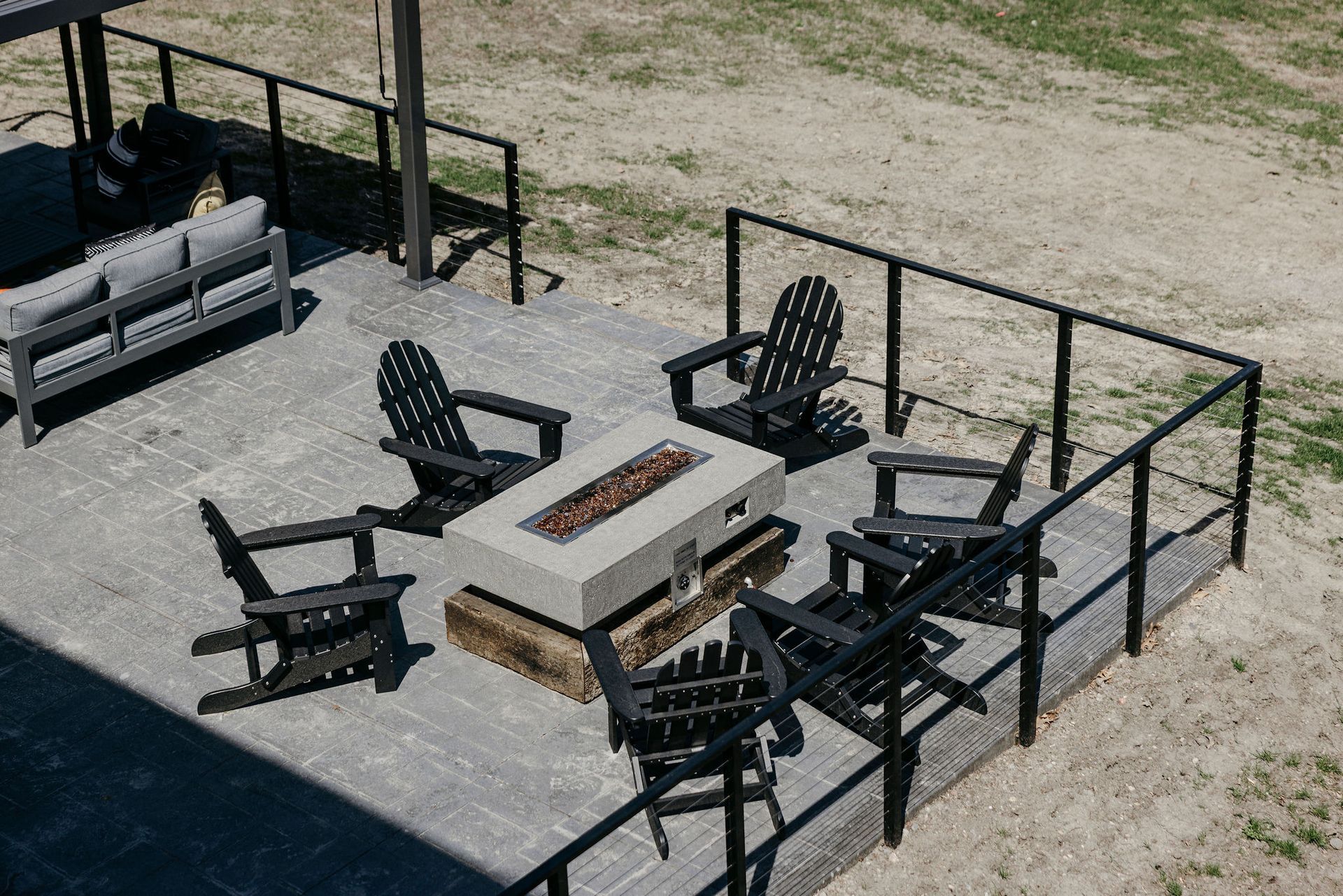 Outdoor patio with black Adirondack chairs around a stone fire pit and fenced seating area