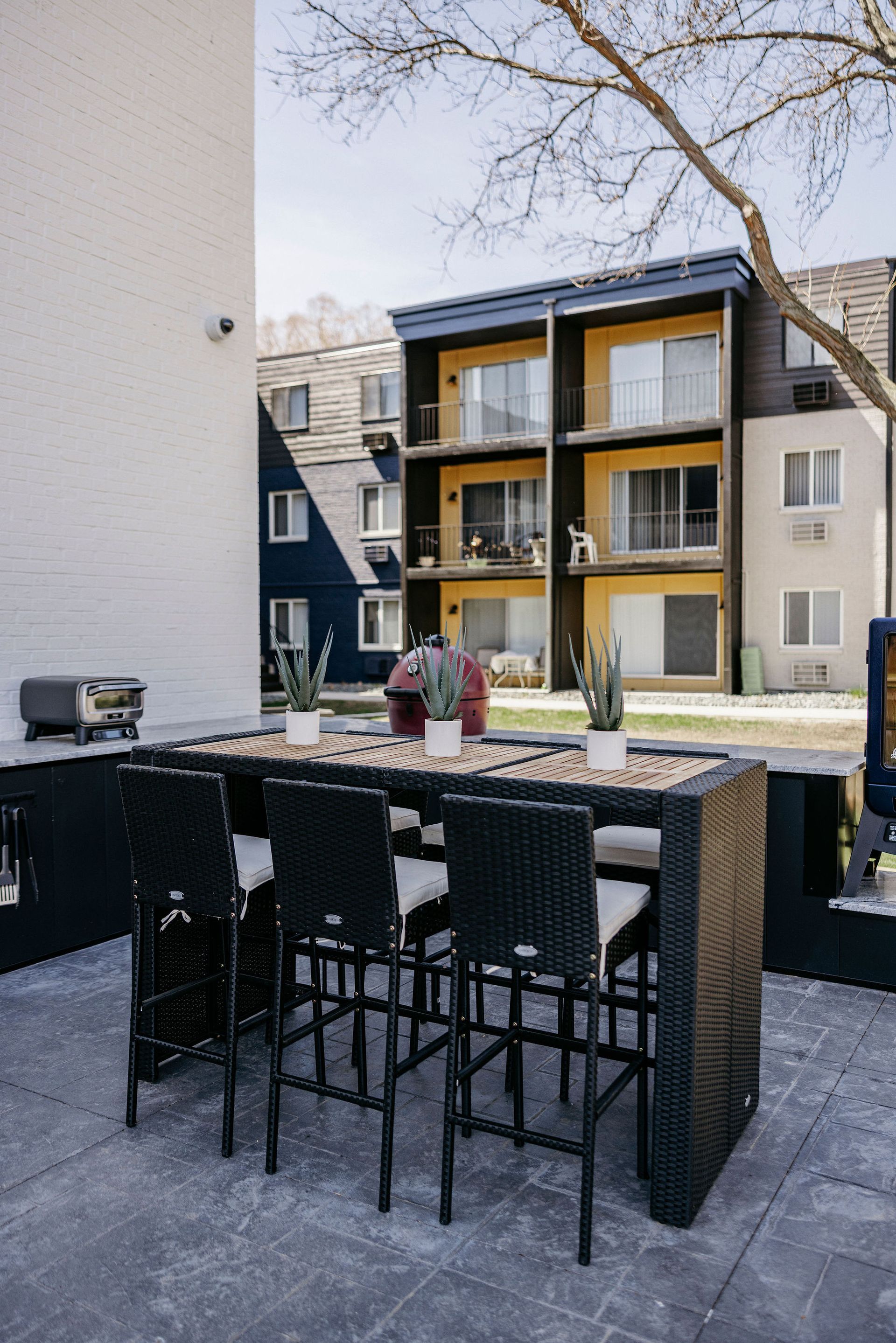Patio with black bar stools and table overlooking an apartment courtyard with a pool and balconies