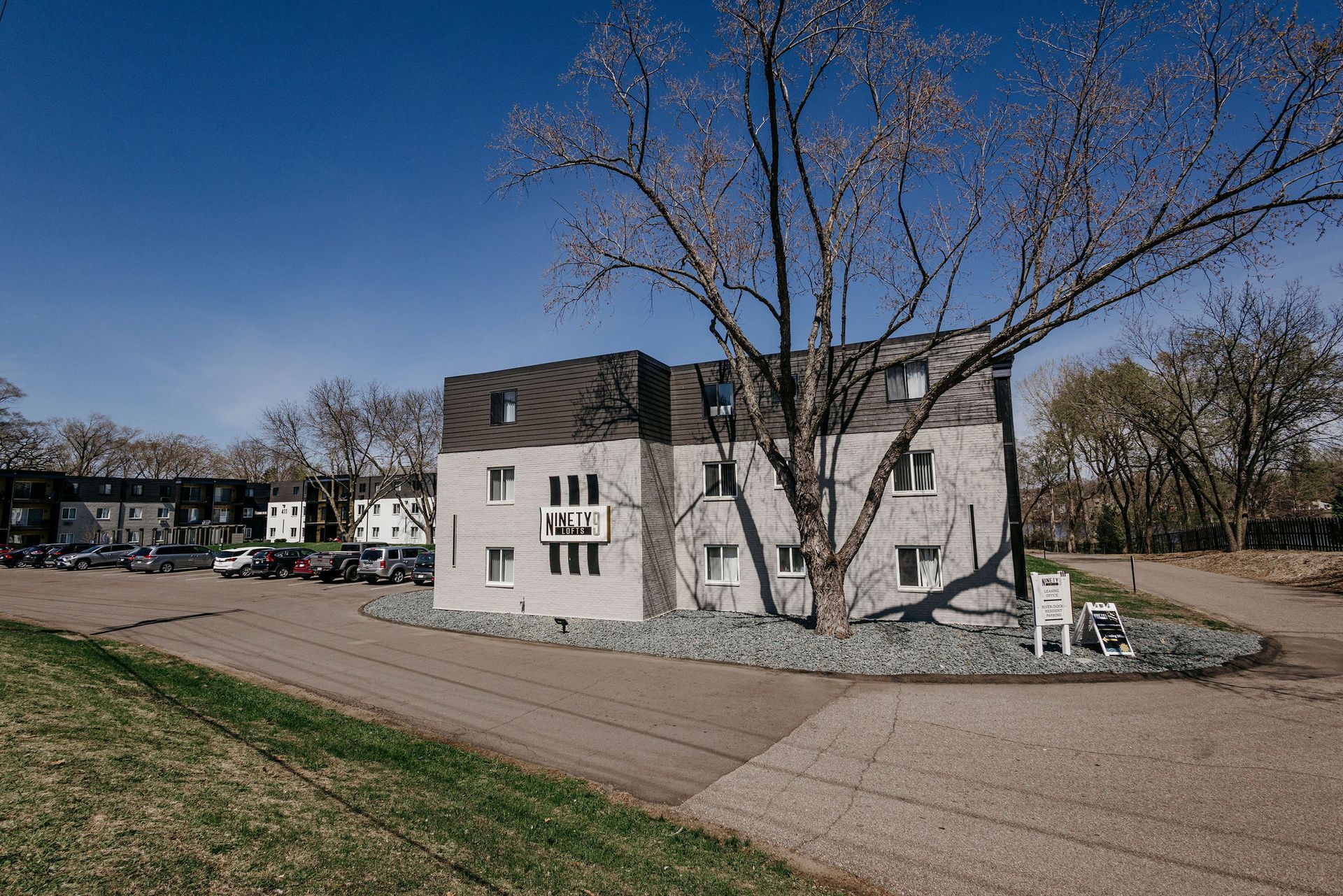 White house with black roof beside a dirt road and leafless tree under a clear blue sky