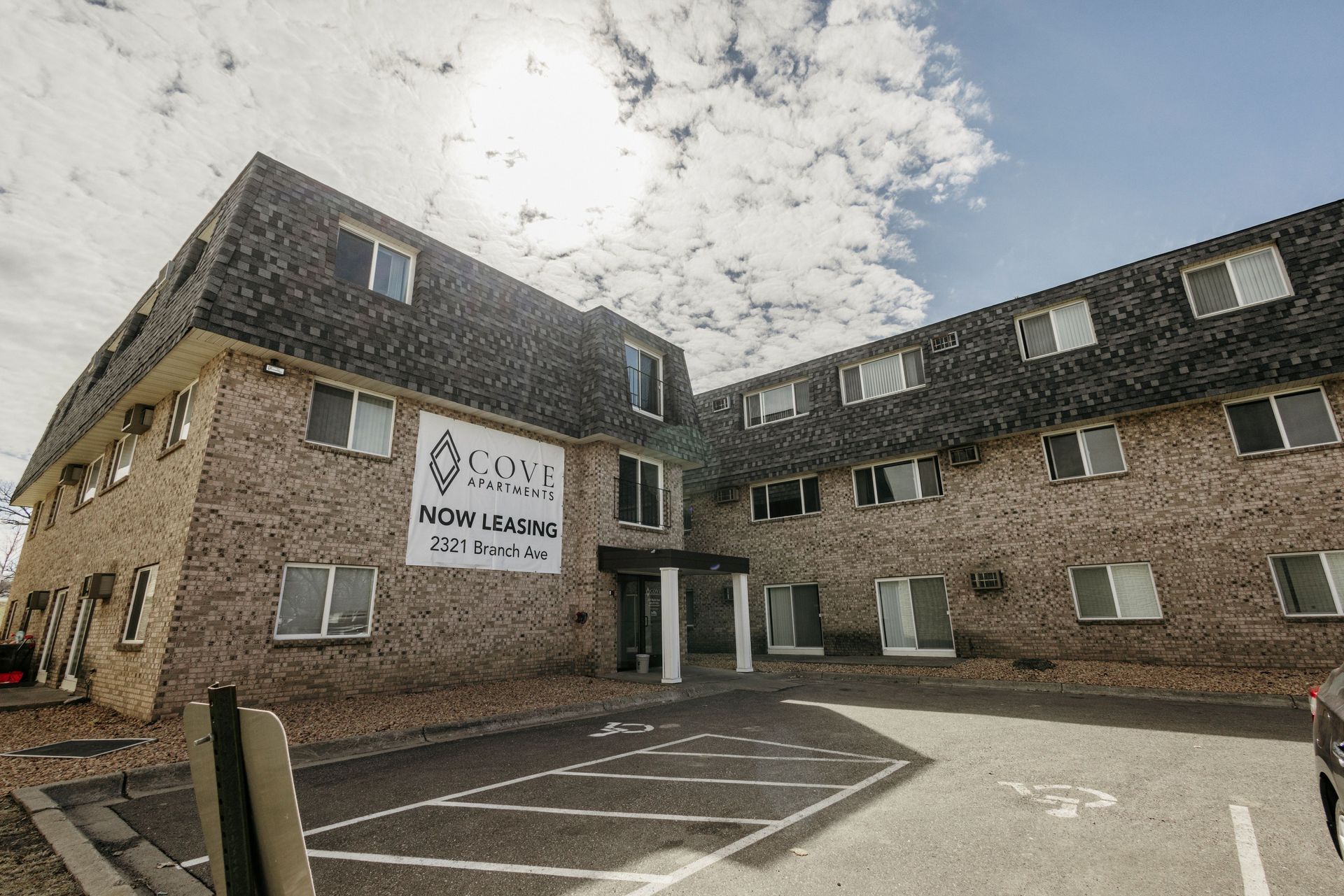 Brick apartment building with a large “Rooms now let” sign and a parking area in front