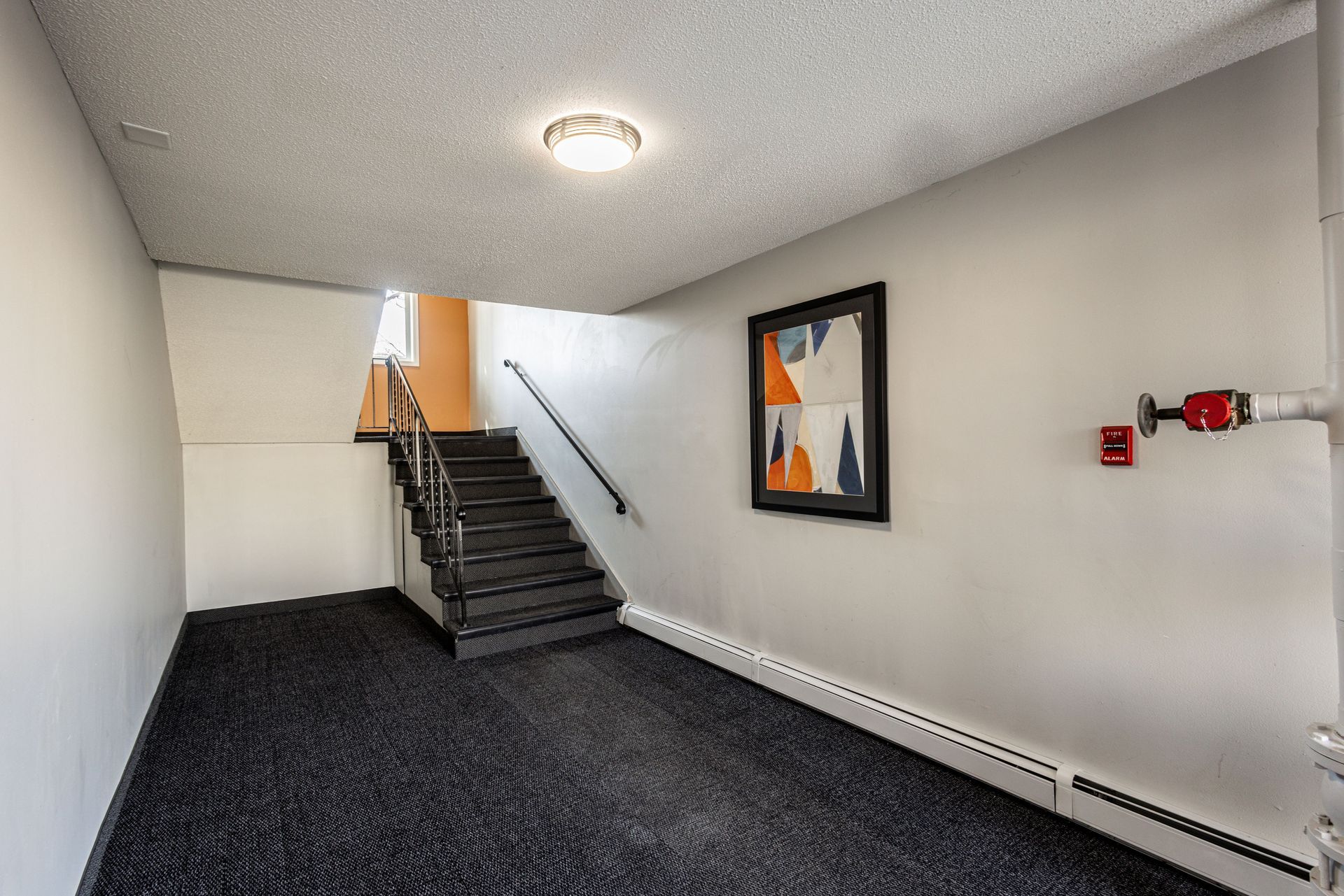 Empty stairwell with black carpeted stairs, white walls, and a framed abstract print.