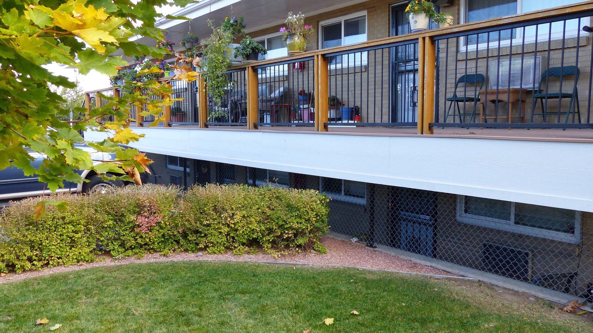 House porch with metal railing, chairs, and a trimmed hedge beside a green lawn.