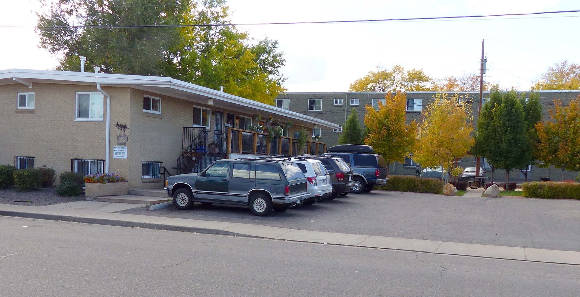 Apartment building with parked cars along a curb on a quiet residential street