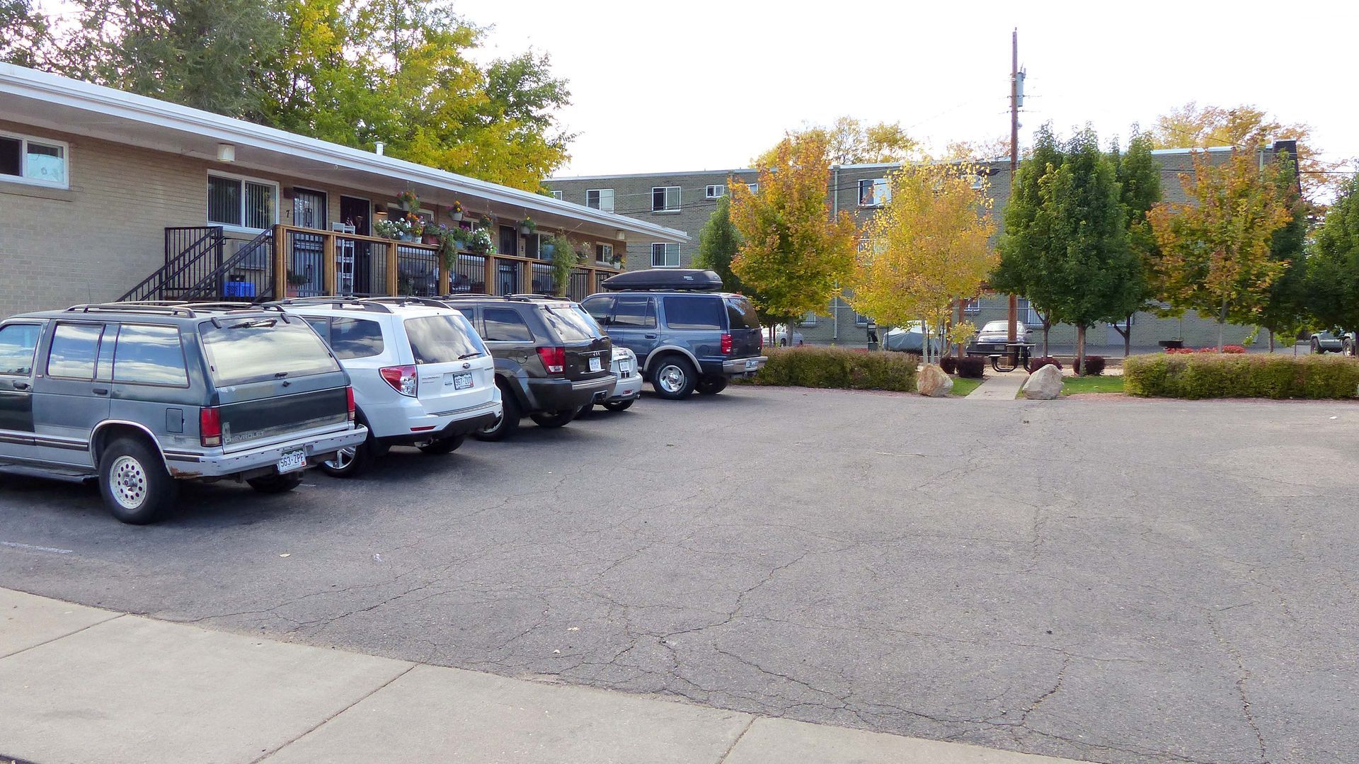 Parking lot outside a low building with several parked cars and autumn trees in front.