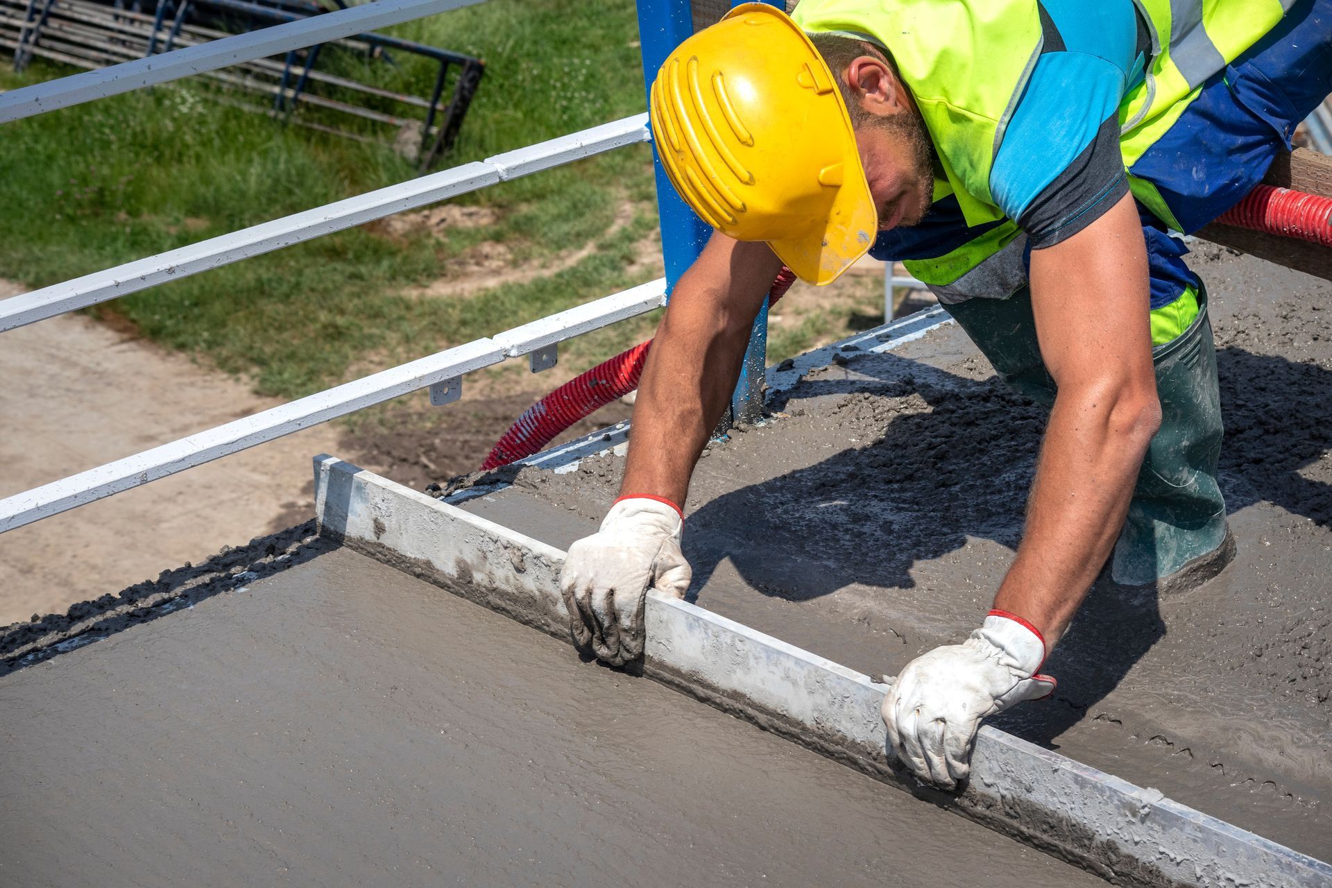 Construction worker in orange safety gear looking at tablet on a job site with other workers and a cement truck.