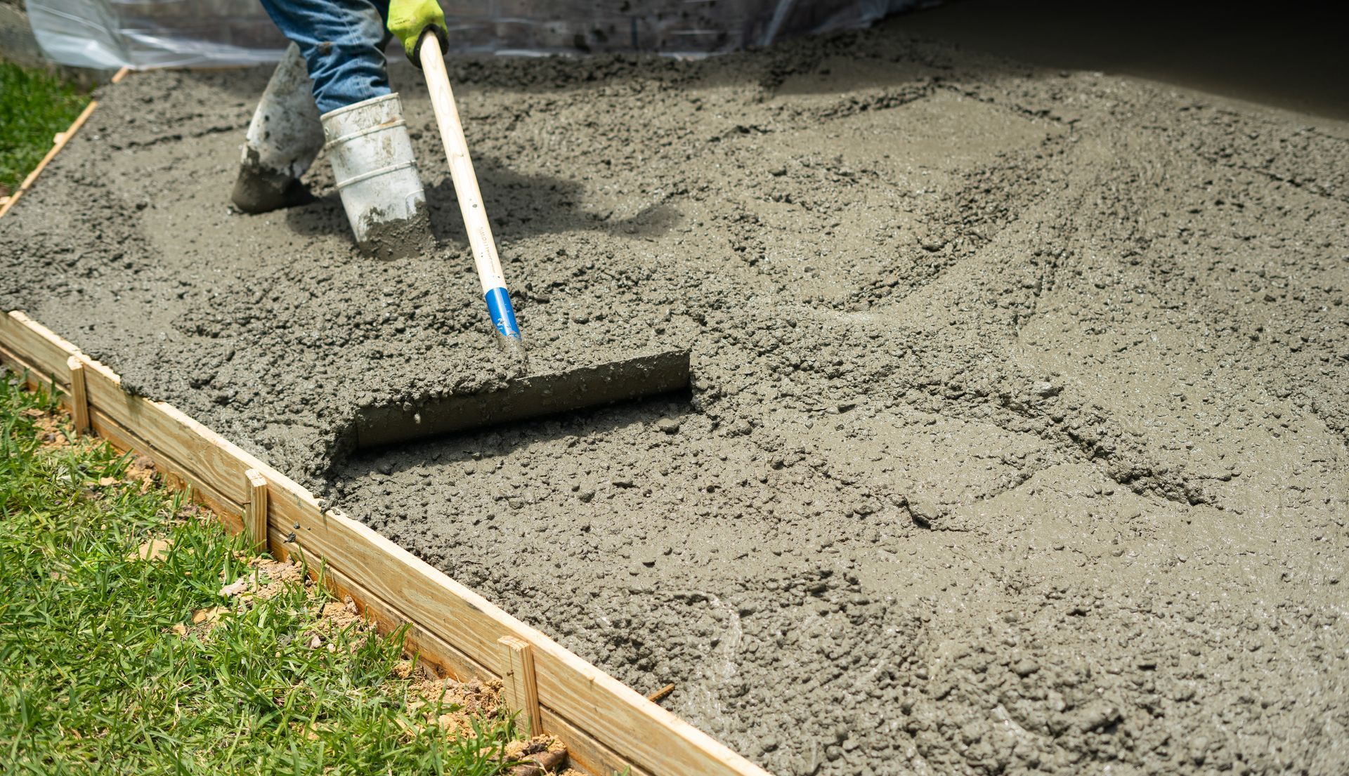 Person leveling wet concrete with a screed tool within wooden forms.