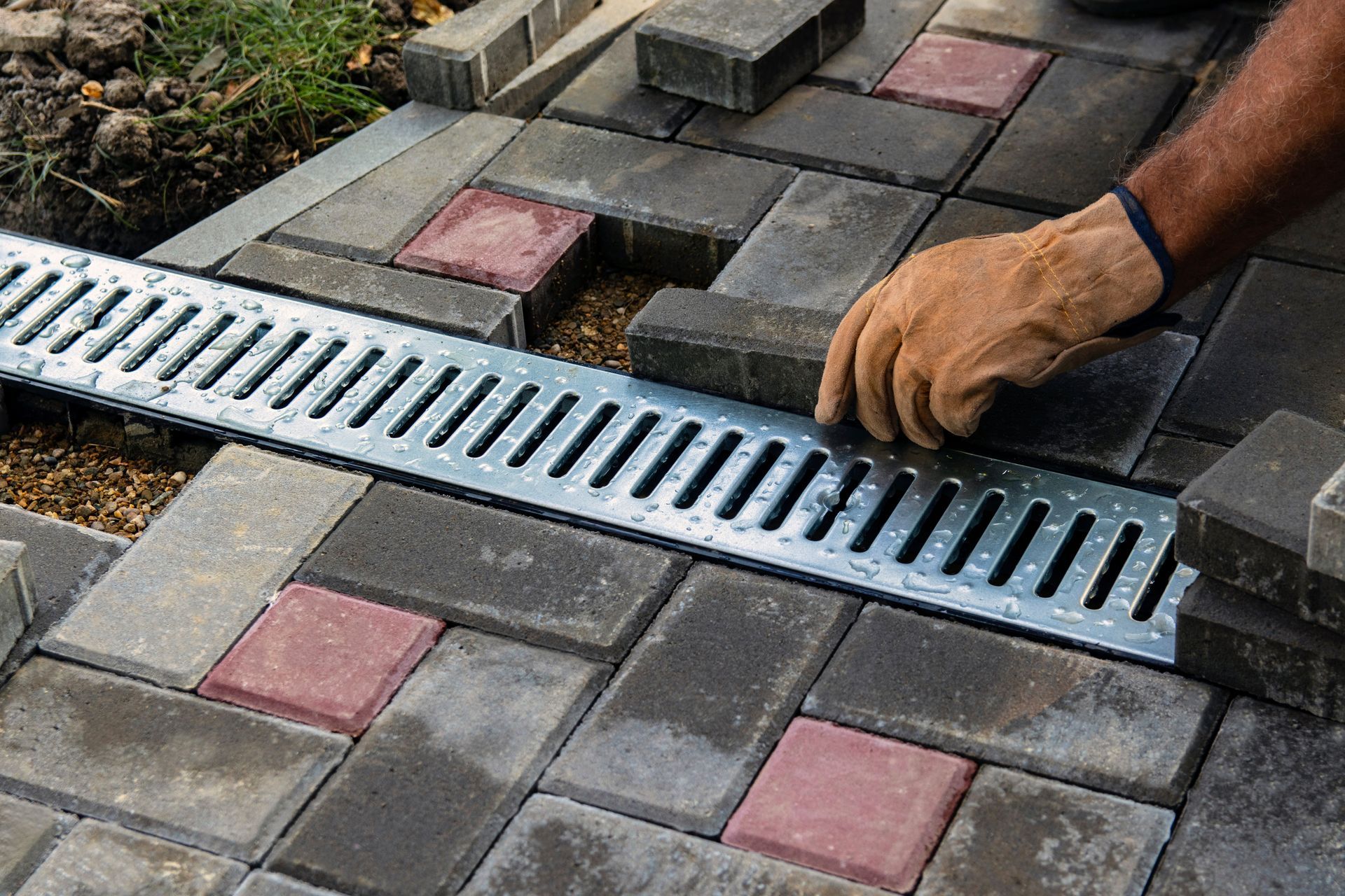Installation of a linear drain with grey and red pavers, worker in gloves placing brick.