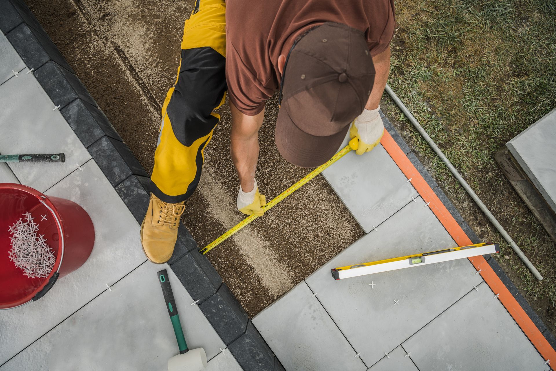 Person measuring paving stones with a tape measure, outdoors.