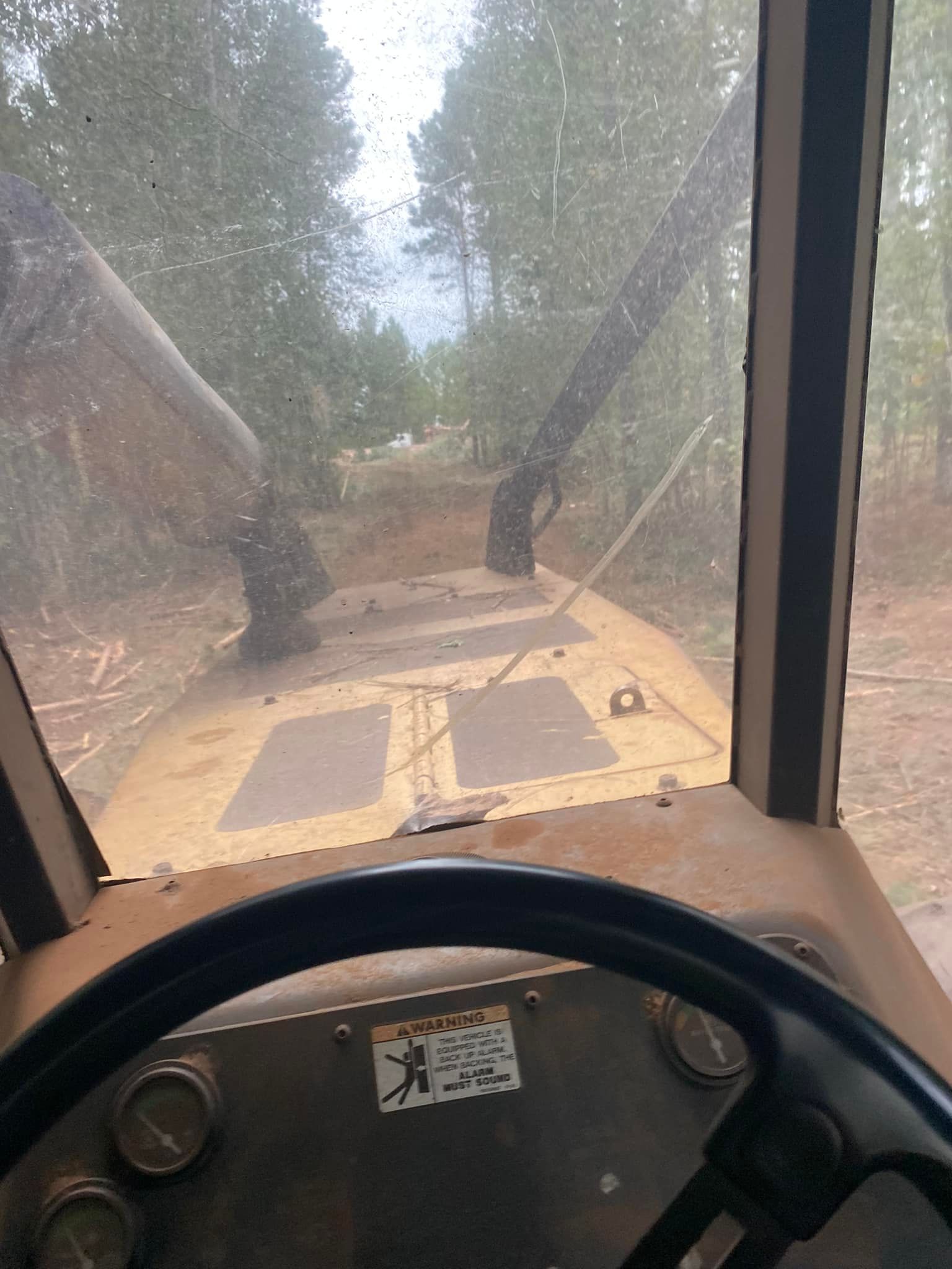 View from the cab of a yellow construction vehicle looking out over a dirt path surrounded by a wooded area.