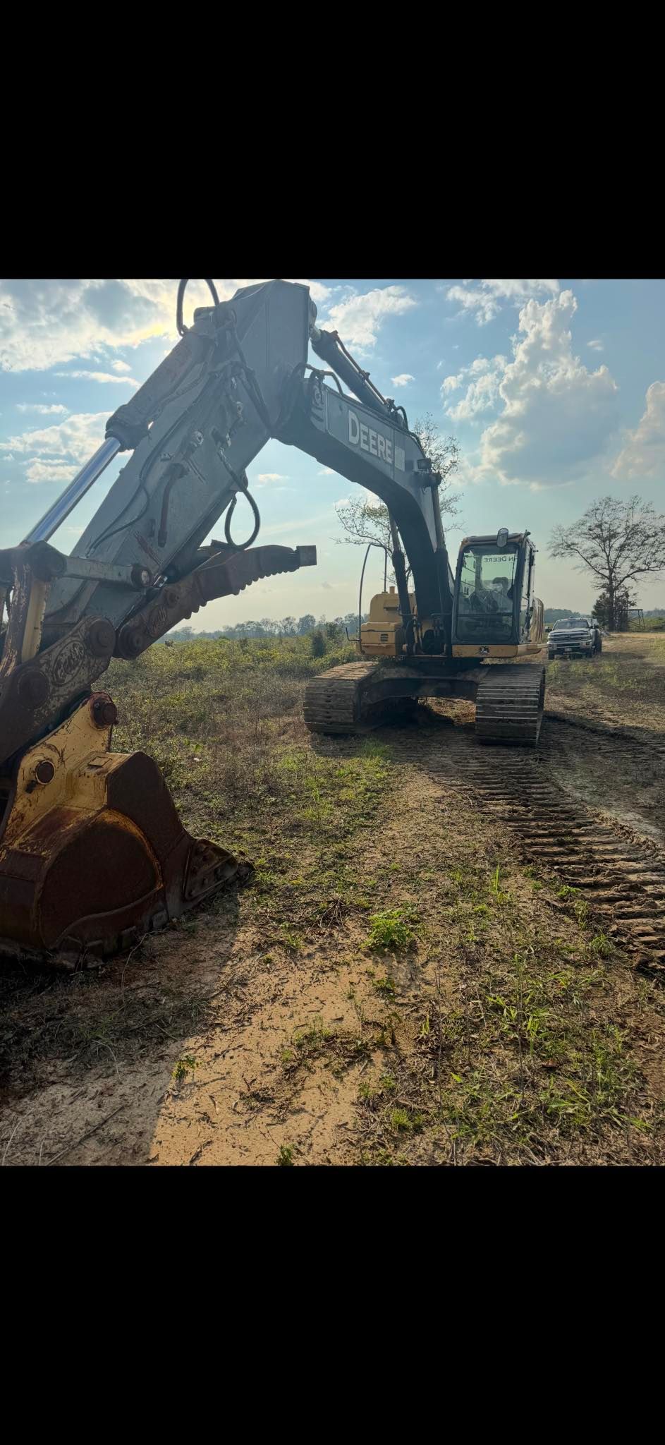 A yellow and black excavator stands in a dirt field under a cloudy sky.