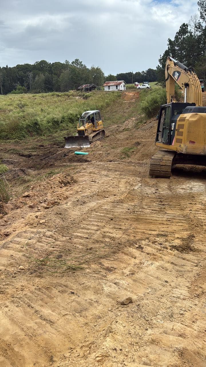A yellow excavator and a bulldozer clearing dirt at an outdoor construction site with a distant building.