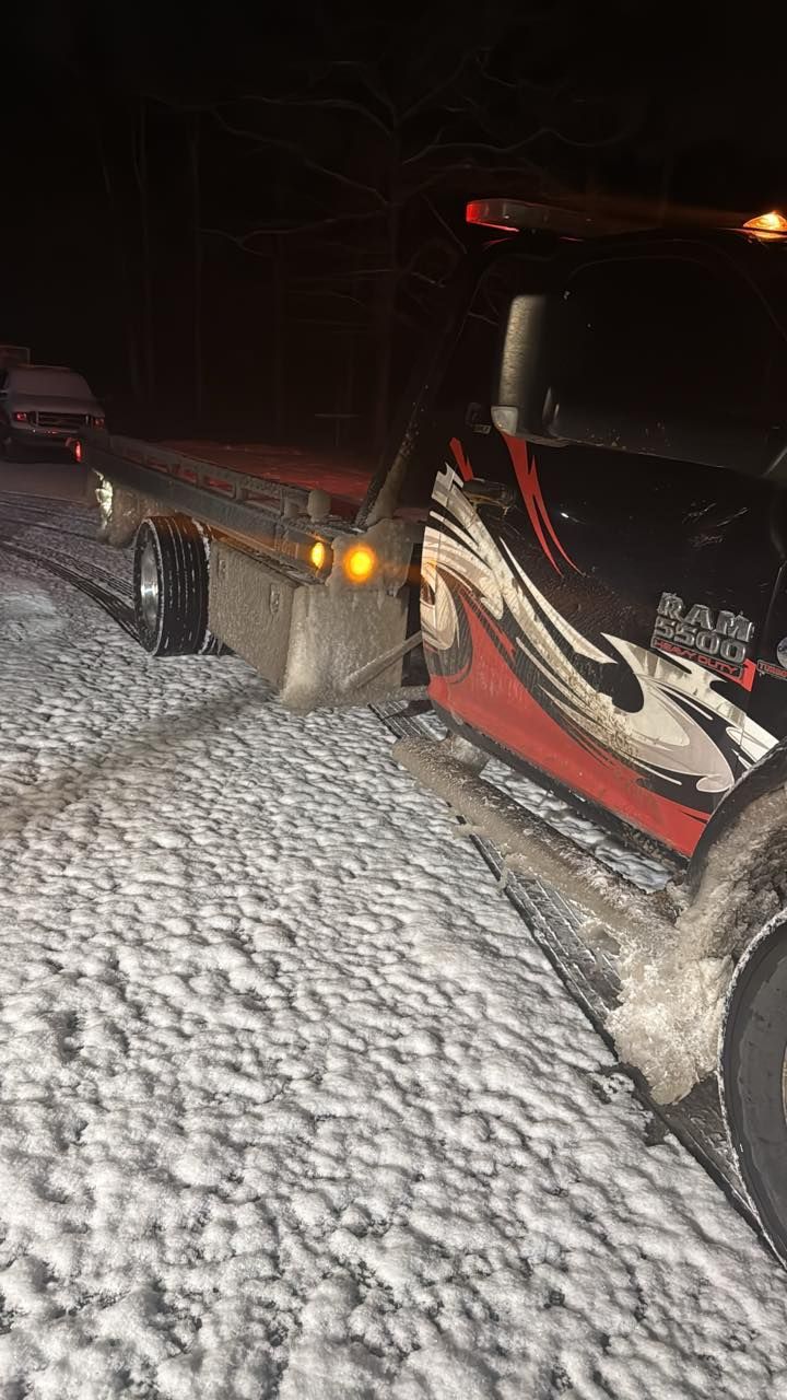 A flatbed tow truck with black and red graphics parked on a snow-covered surface at night.