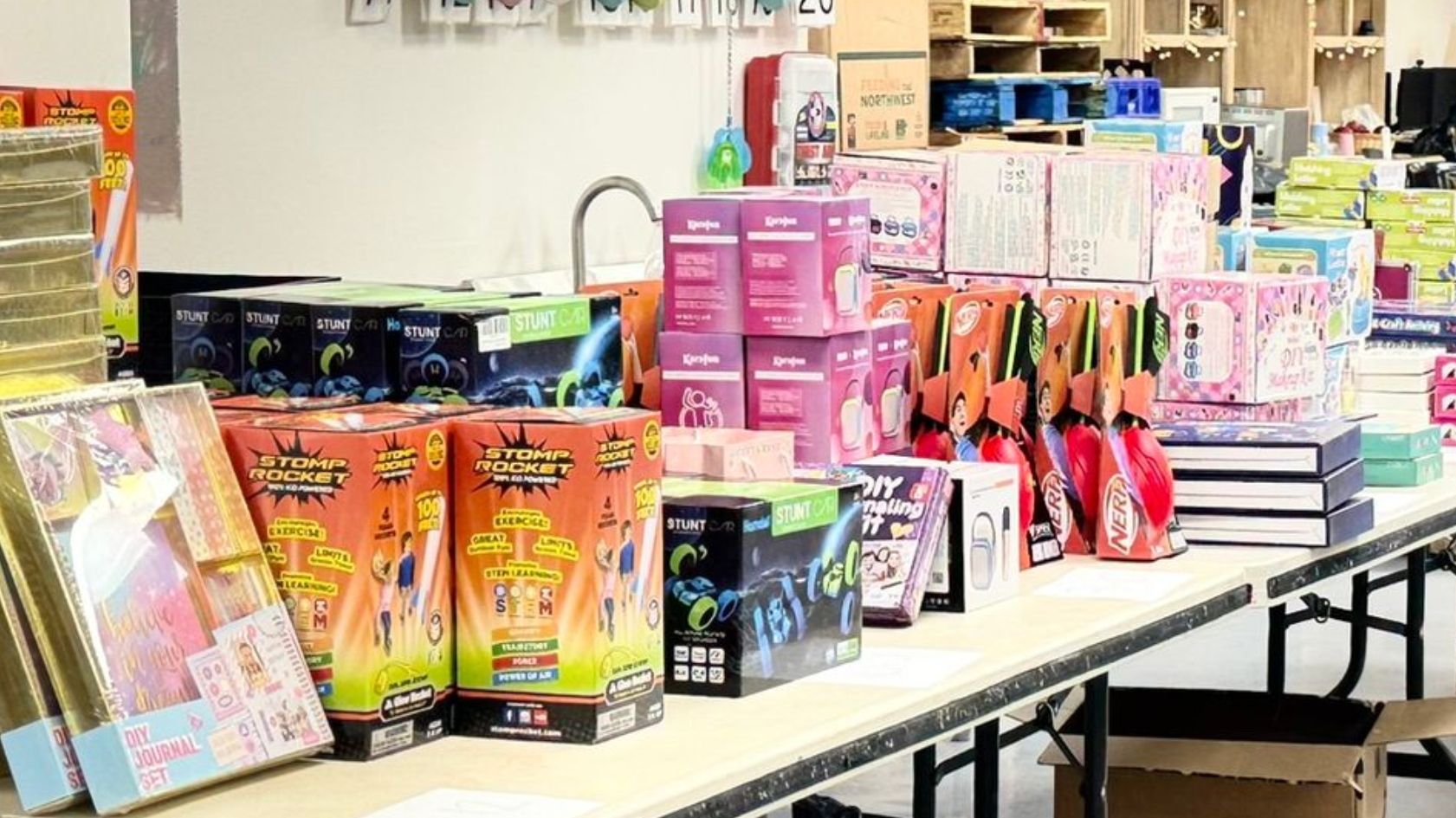 A table filled with various boxed children’s toys, games, and activity kits, displayed in an indoor storage or shop area.