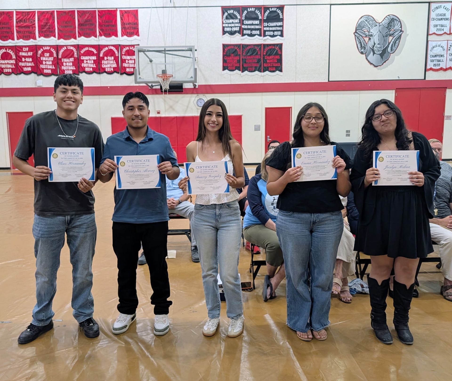Six people stand in a line on a gymnasium floor, each holding a small card while facing the camera.